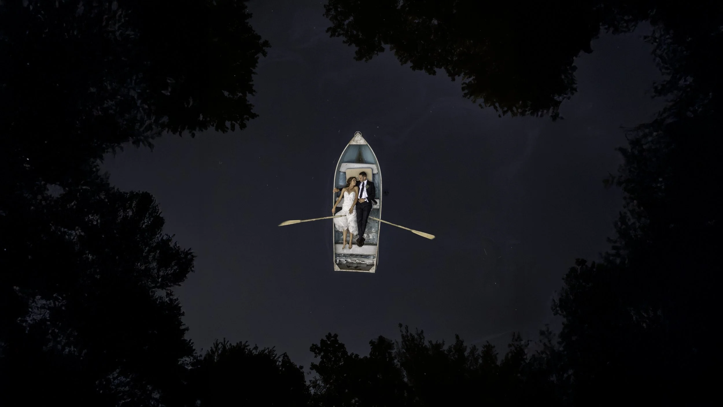 Dramatic aerial drone photograph of a wedding couple laying in a row boat  in Niagara.jpg