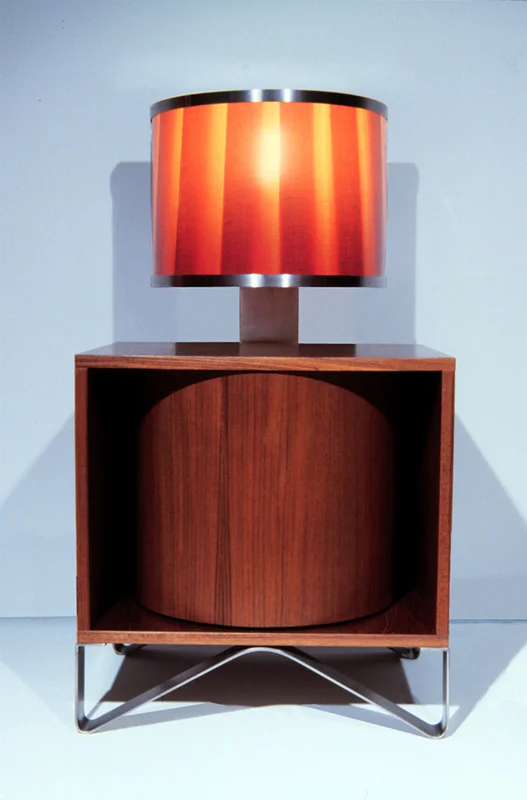   Utsurio Bedside Tables   Teak Veneer + Photographic Film + Aluminum Frame 36”H X 30”W X 30”D  The stripey shade is an enlarged photograph of a traditional fabric lampshade.&nbsp; The cylindrical shelving element can be rotated to hide, reveal or pa