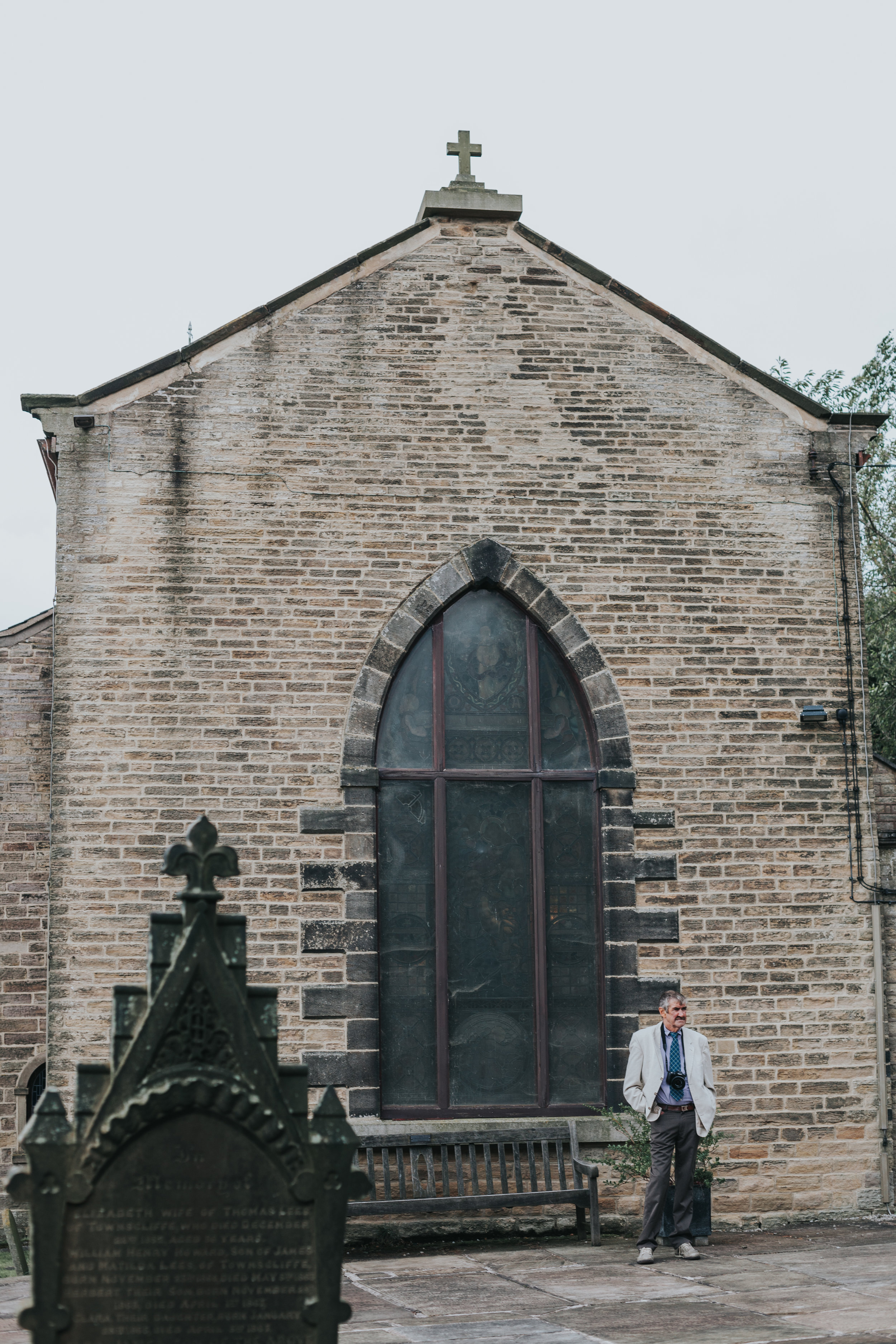  Man stands outside church with camera around his neck.&nbsp; 