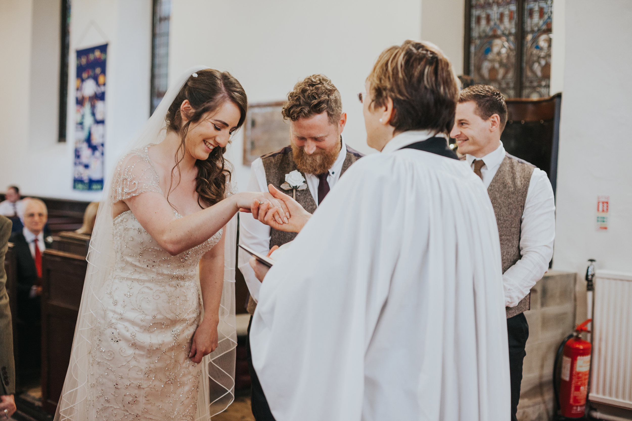  Female vicar holds bride's hand. Bride laughs.&nbsp; 