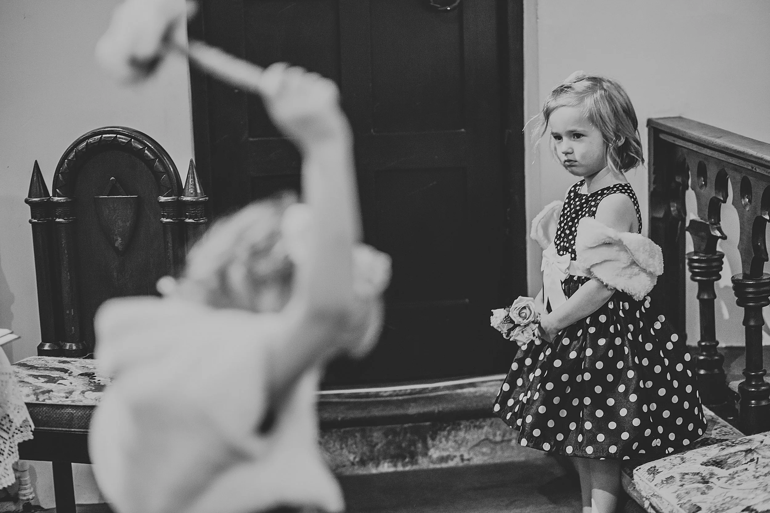 Grumpy child is back to being grumpy again while other child wheels hammer in foreground... or paper flowers, she's artfully out of focus so it's hard to tell. 