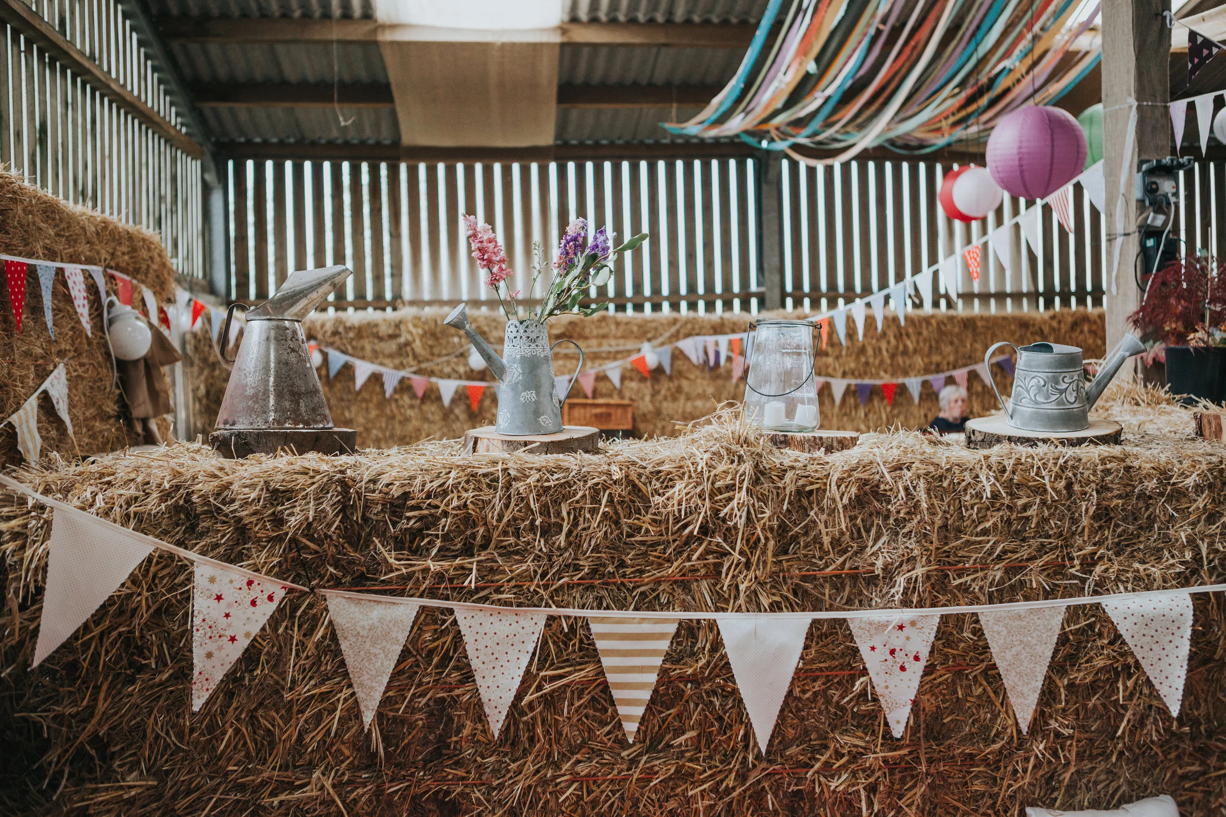 Silver watering cans holding flowers, bunting and coloured streamers.