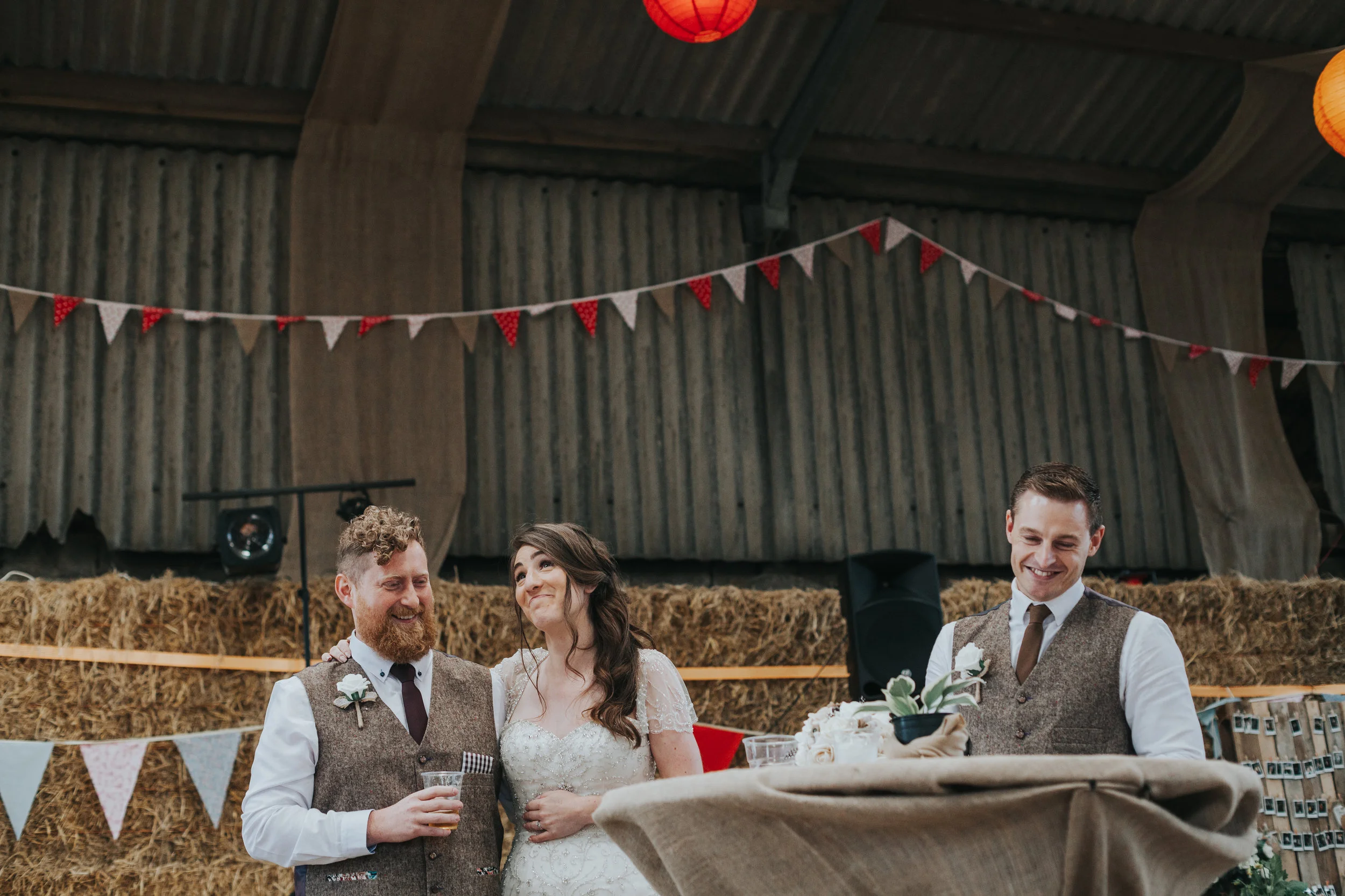 Bride pulls playful knowing face while groom and best man laugh, during best mans speech