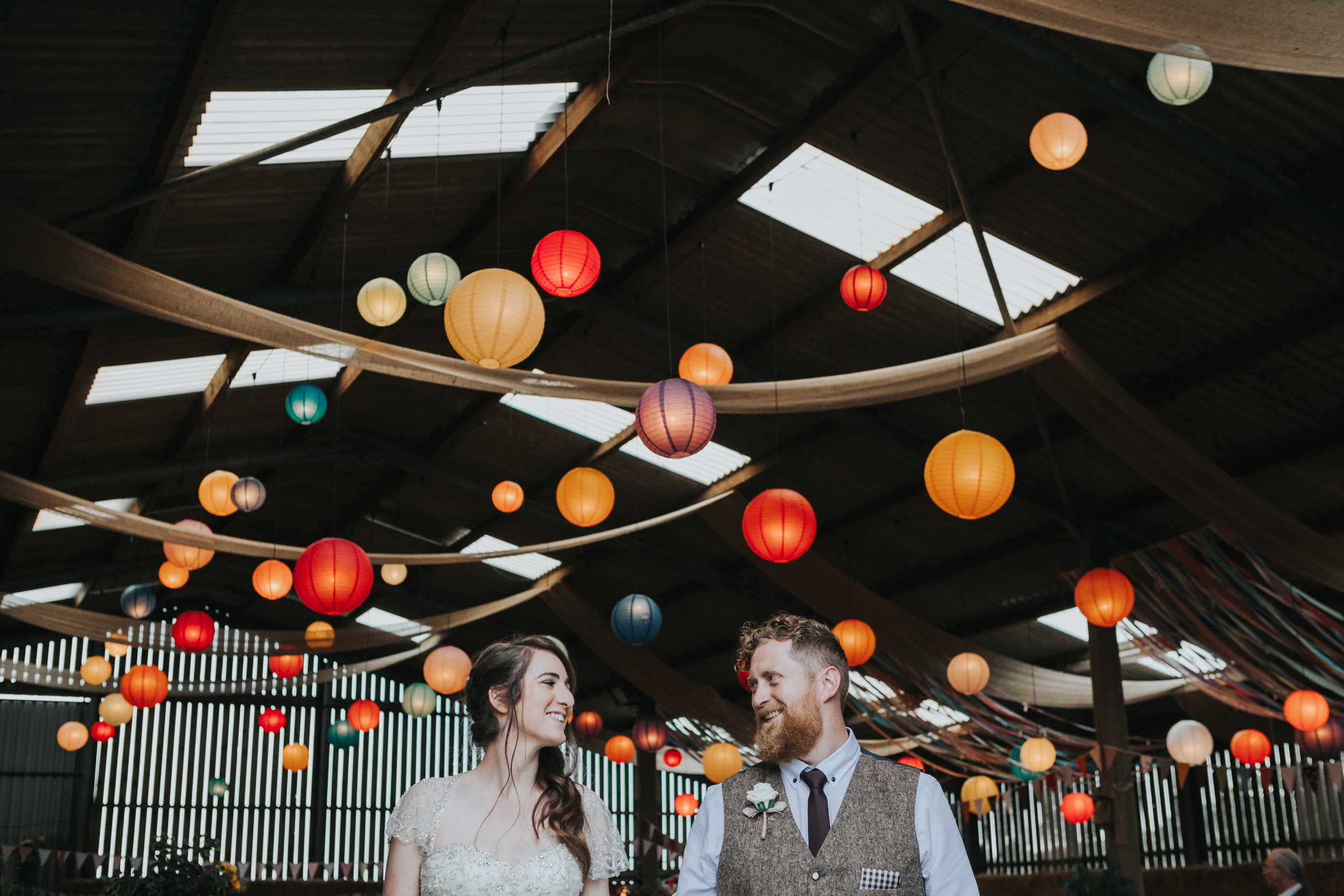  Bride and Groom stand together in front of room full of colourful lanterns&nbsp; 