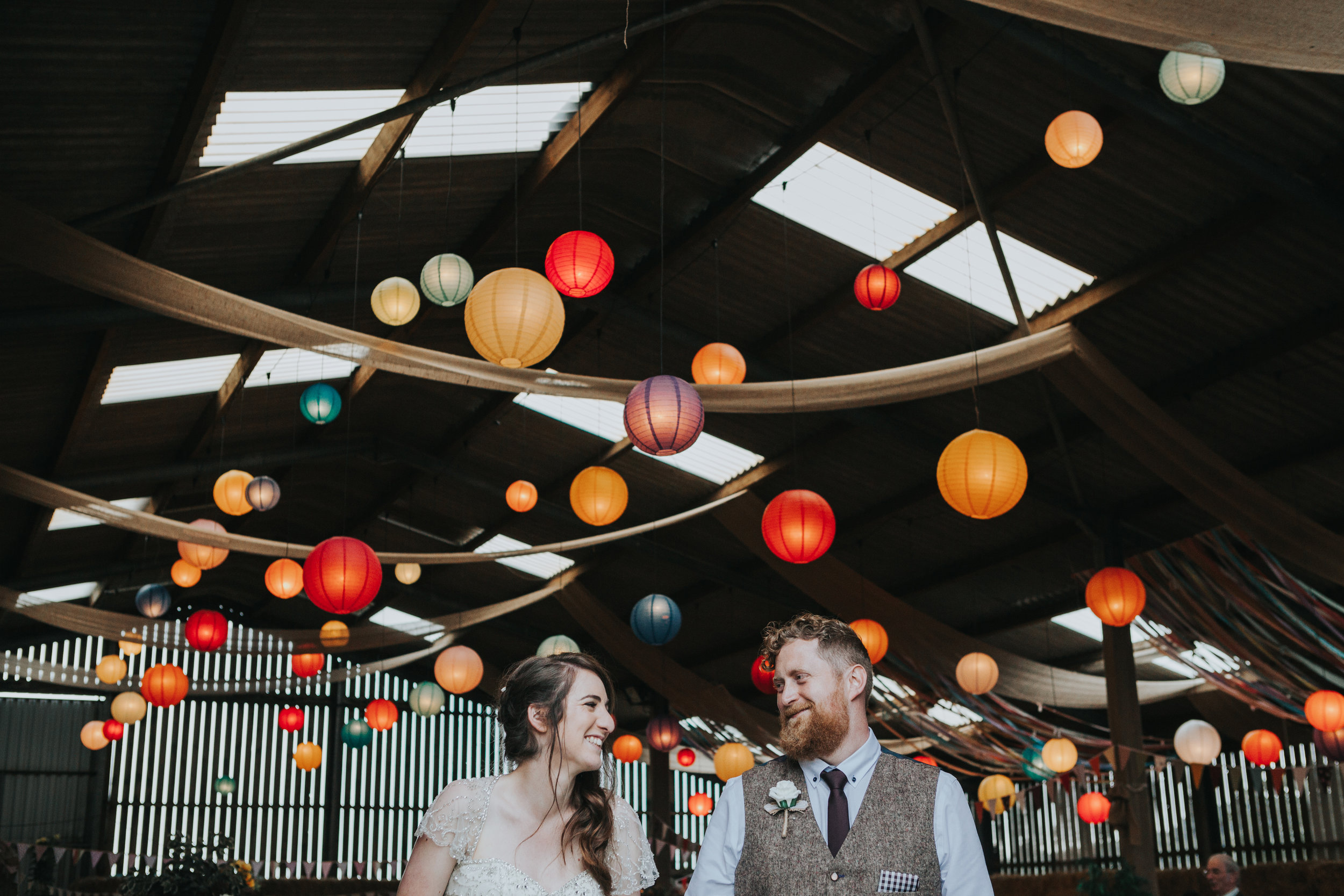  Bride and Groom stand together in front of room full of colourful lanterns that they put there together the day before 