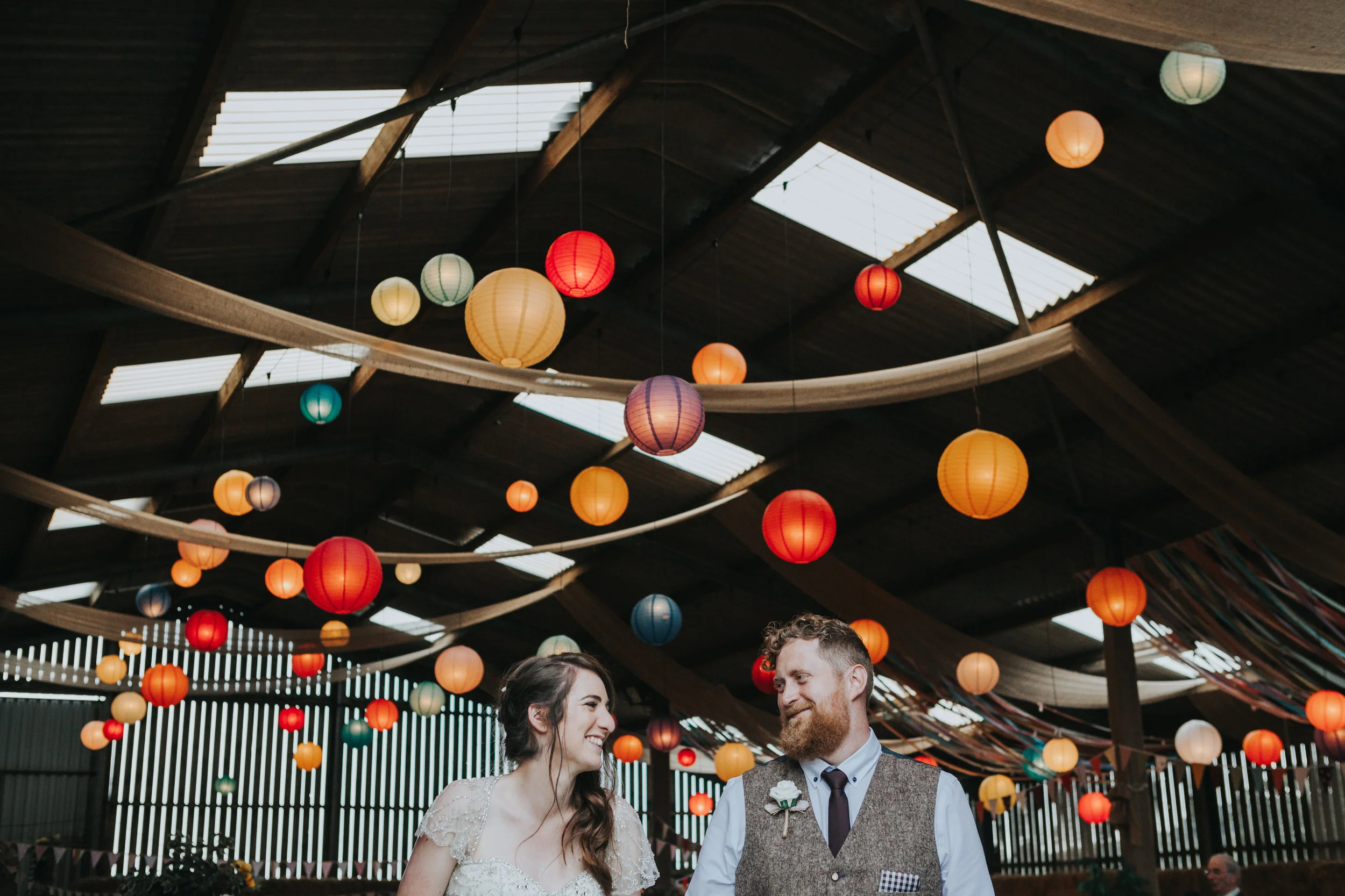 Bride and Groom stand together in front of room full of colourful lanterns that they put there together the day before