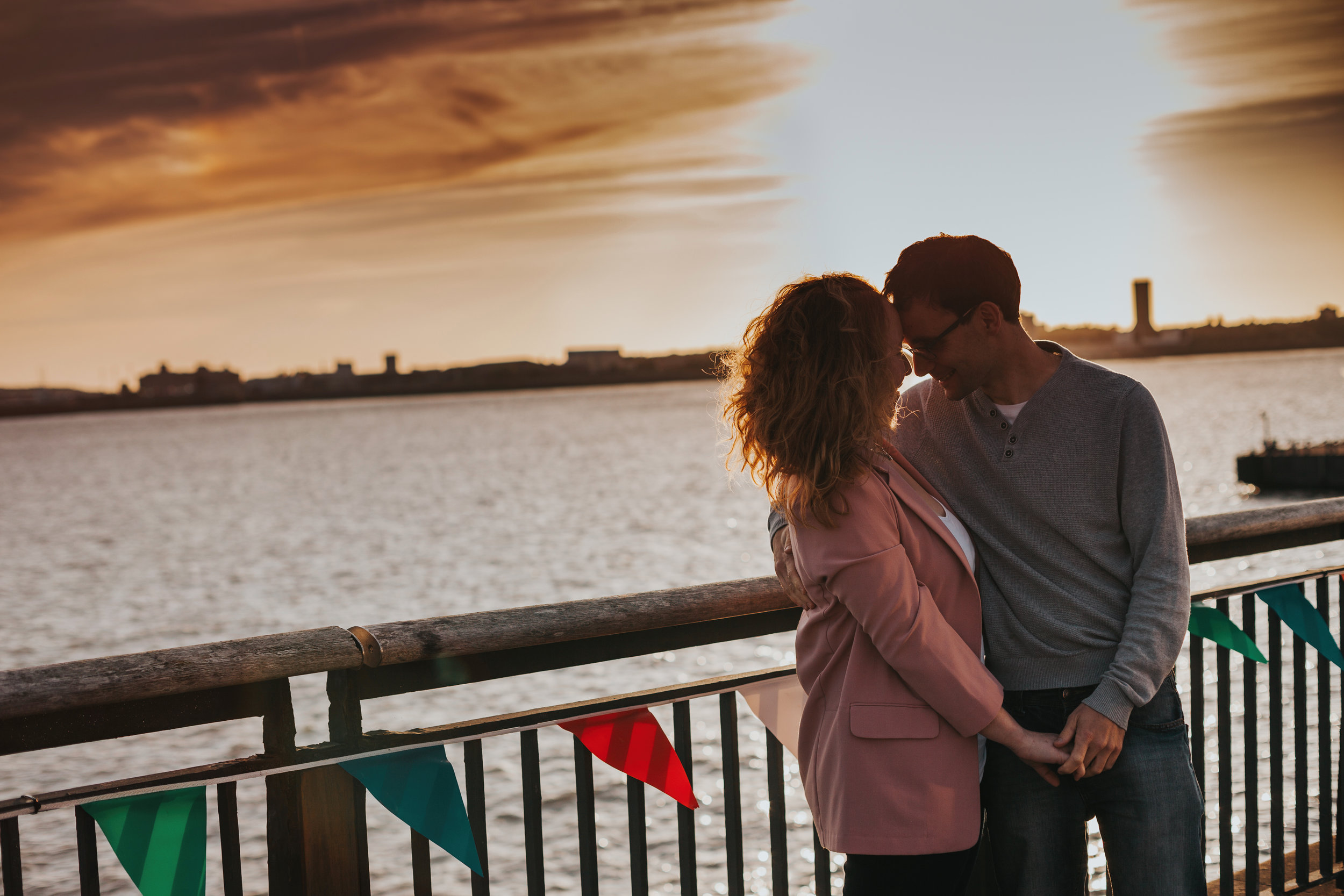 Couples heads together, sun setting behind them. 