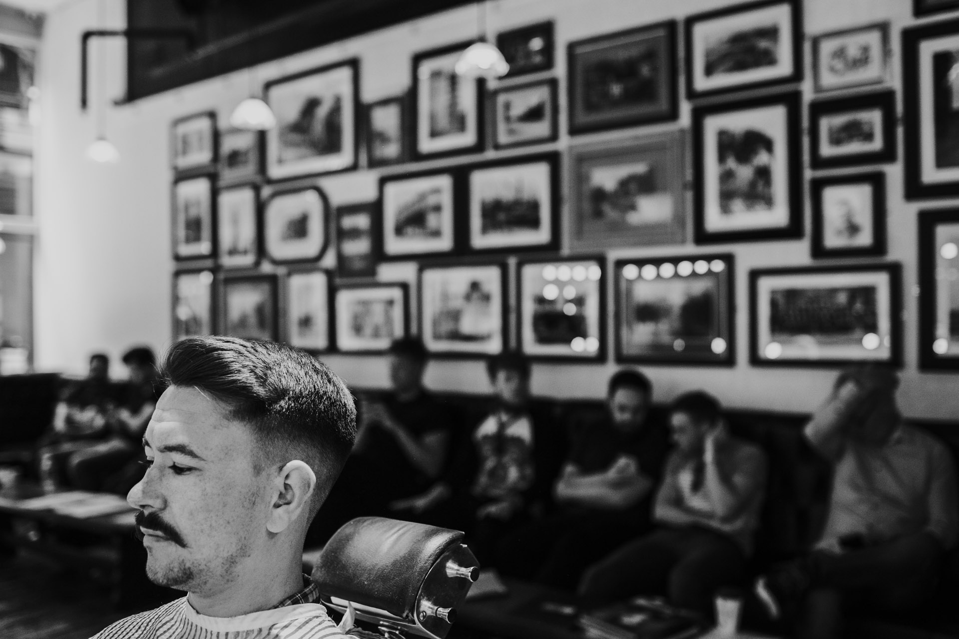 Black and white photograph of groom in front of a wall full of pictures. 