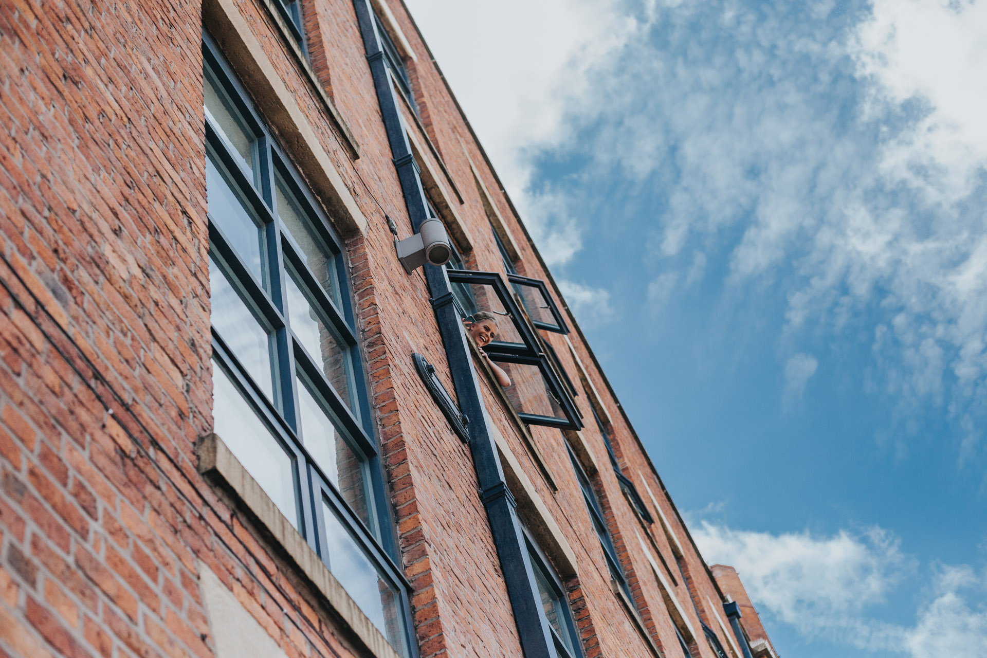 Bride hanging out of the window of their Manchester apartment