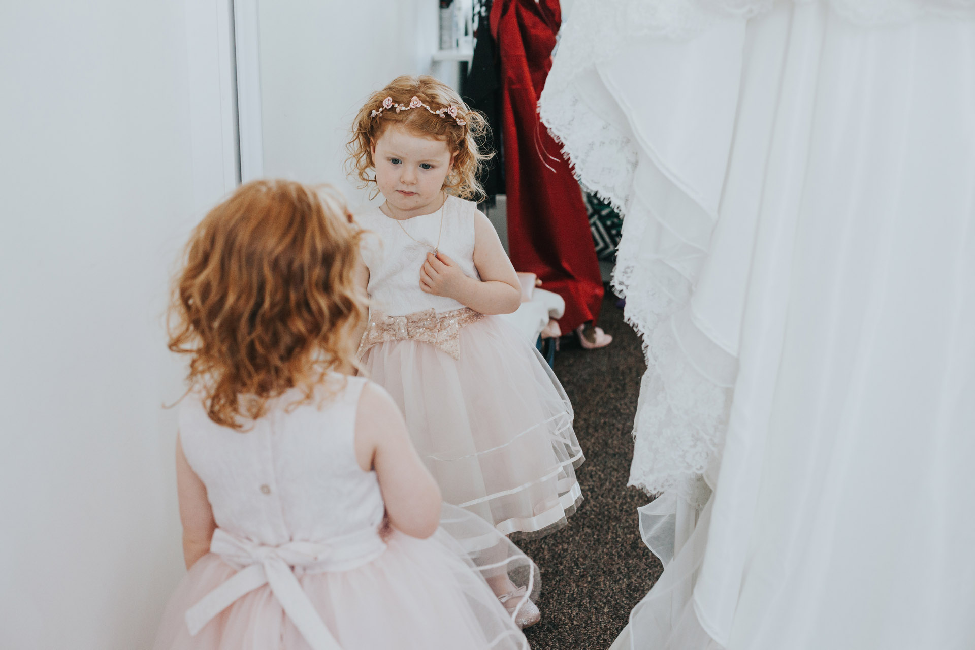 Flower girl looks at her self in the mirror in her special dress.