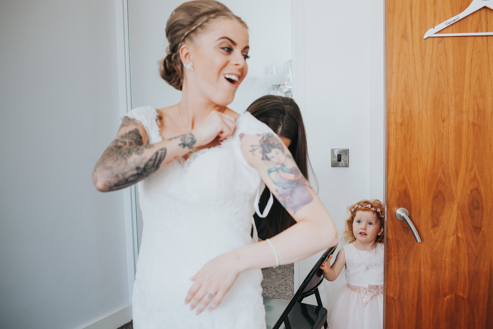 Bride shares a laugh with her bridesmaids as she puts on her wedding dress.