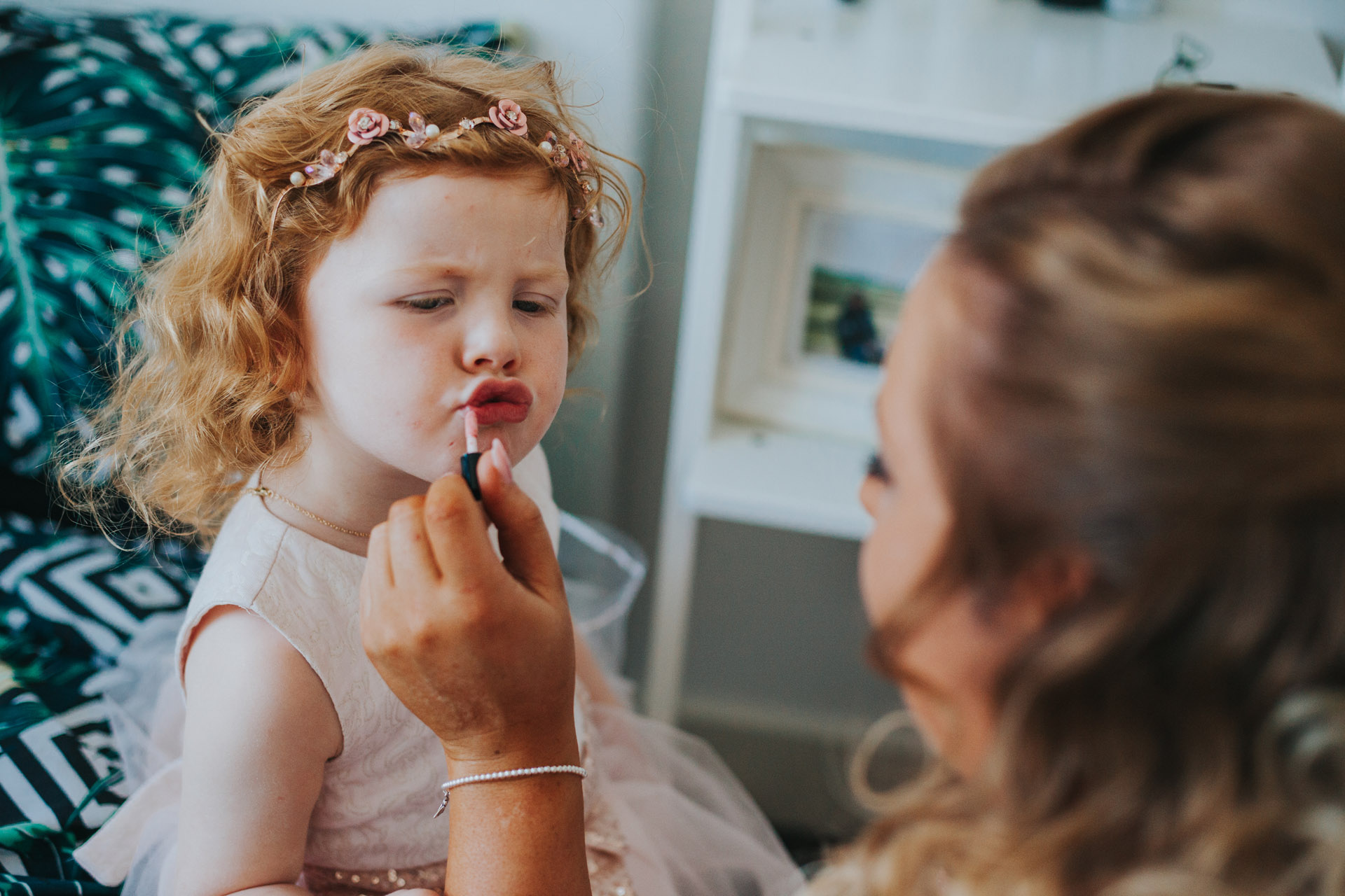 Flower girl pulls a funny pouty face as the bridesmaid puts lipstick on her.