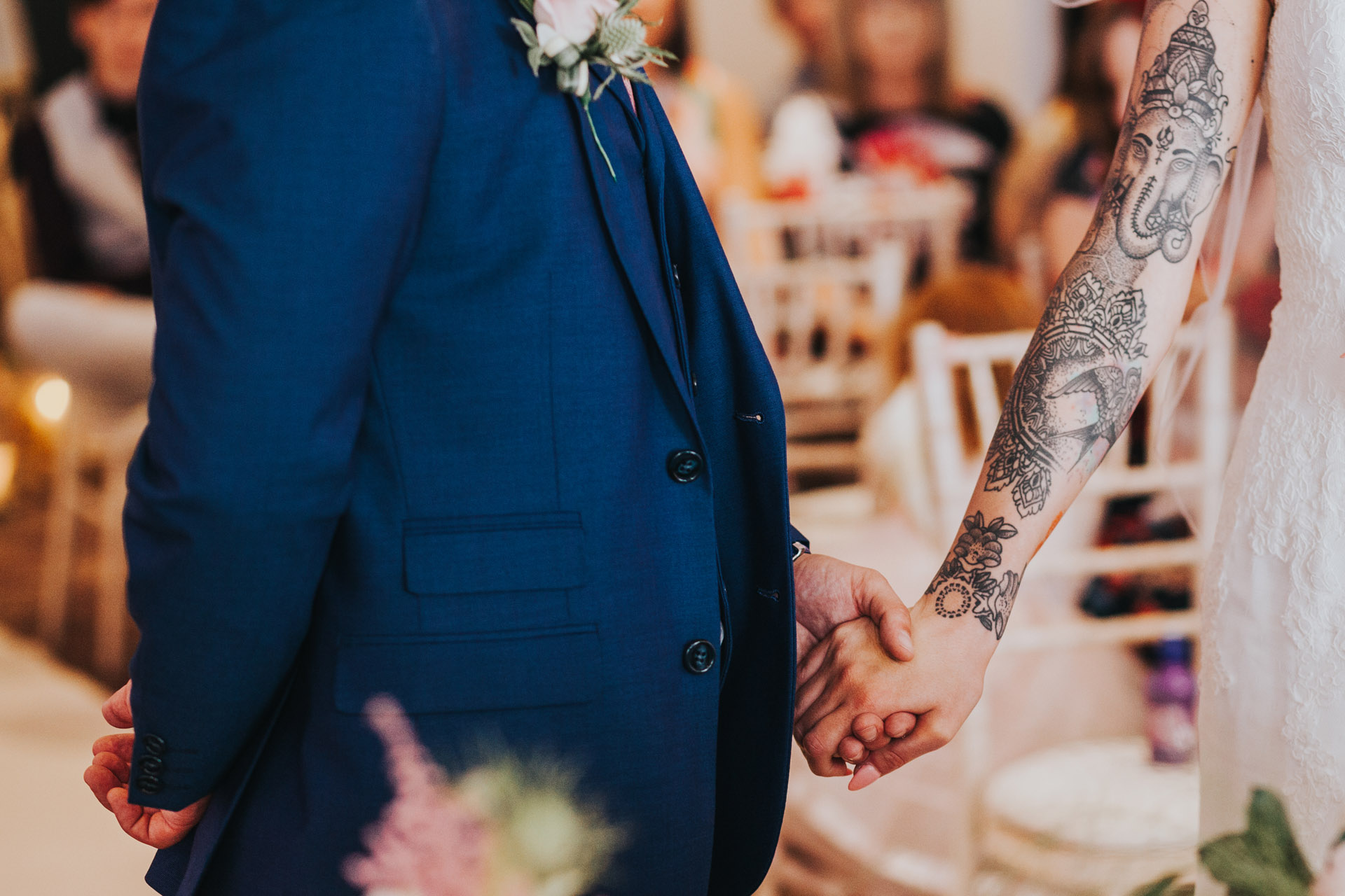 Brides beautiful tattooed arm stretches out to hold grooms hand. Close up photograph. 