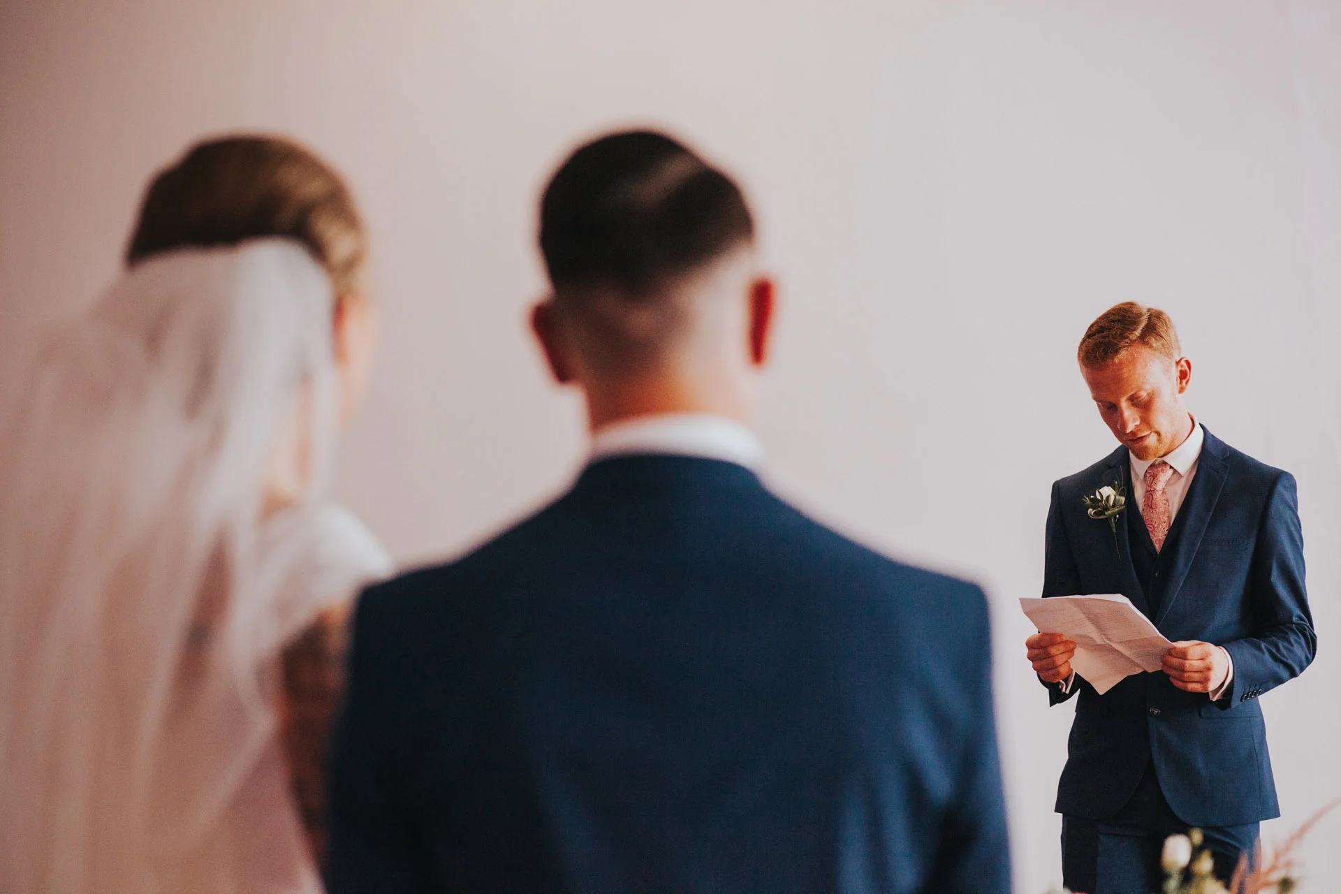 A friend reads a reading as the bride and groom watch him. 