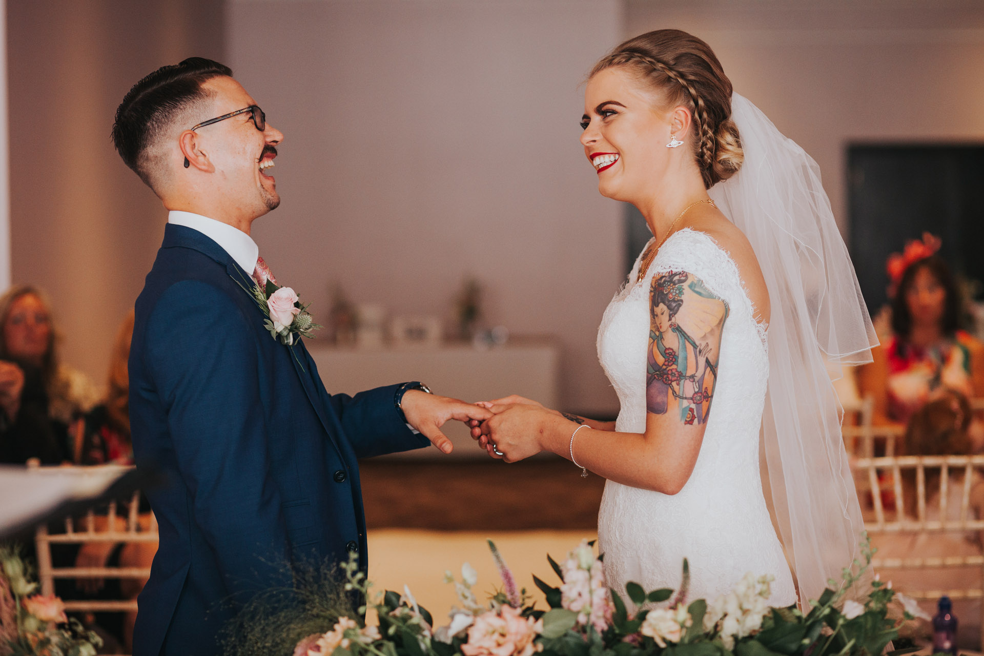 Groom laughs as bride puts on his ring. 