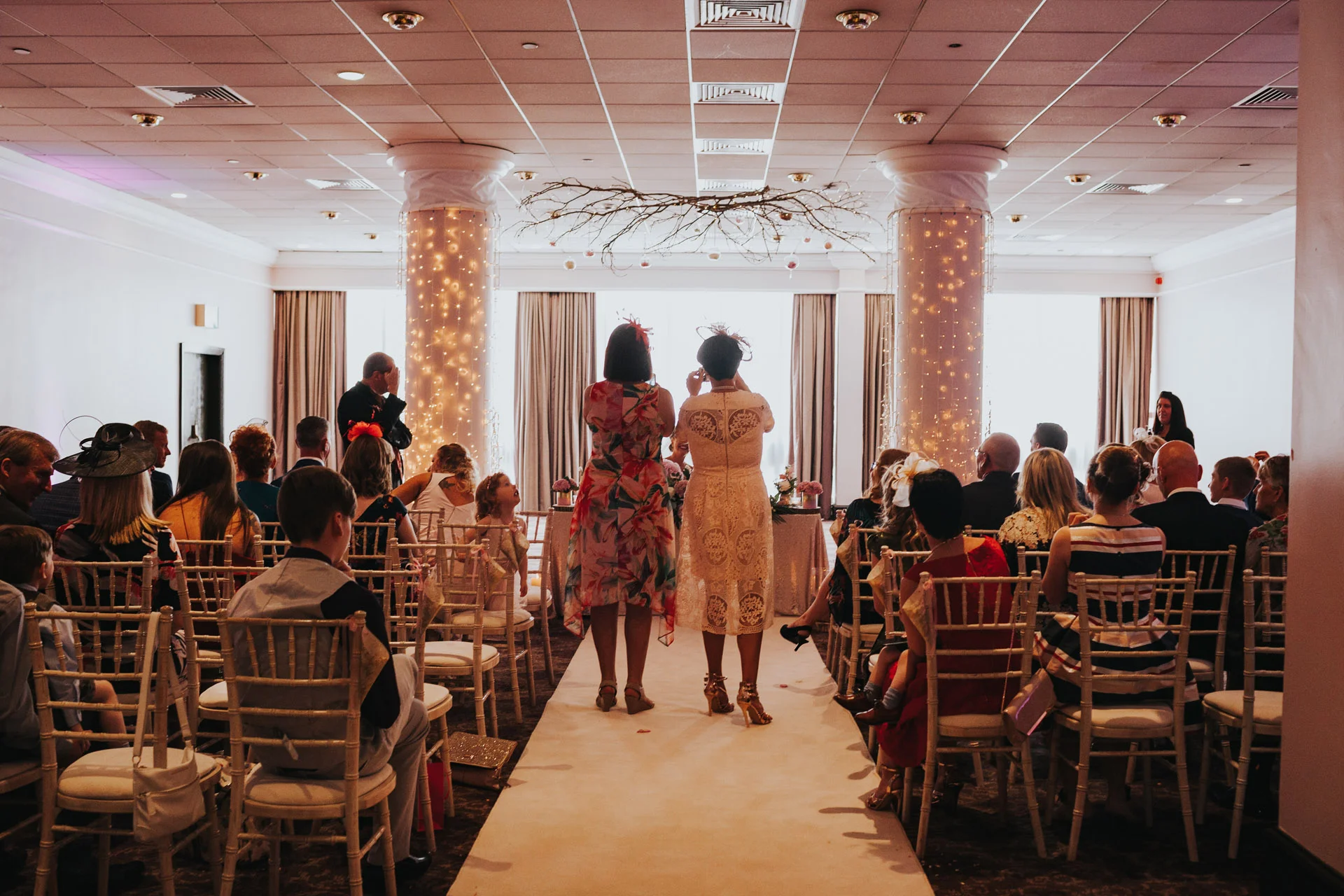 Two guests take photographs of the Bride and Groom signing the registrar. 