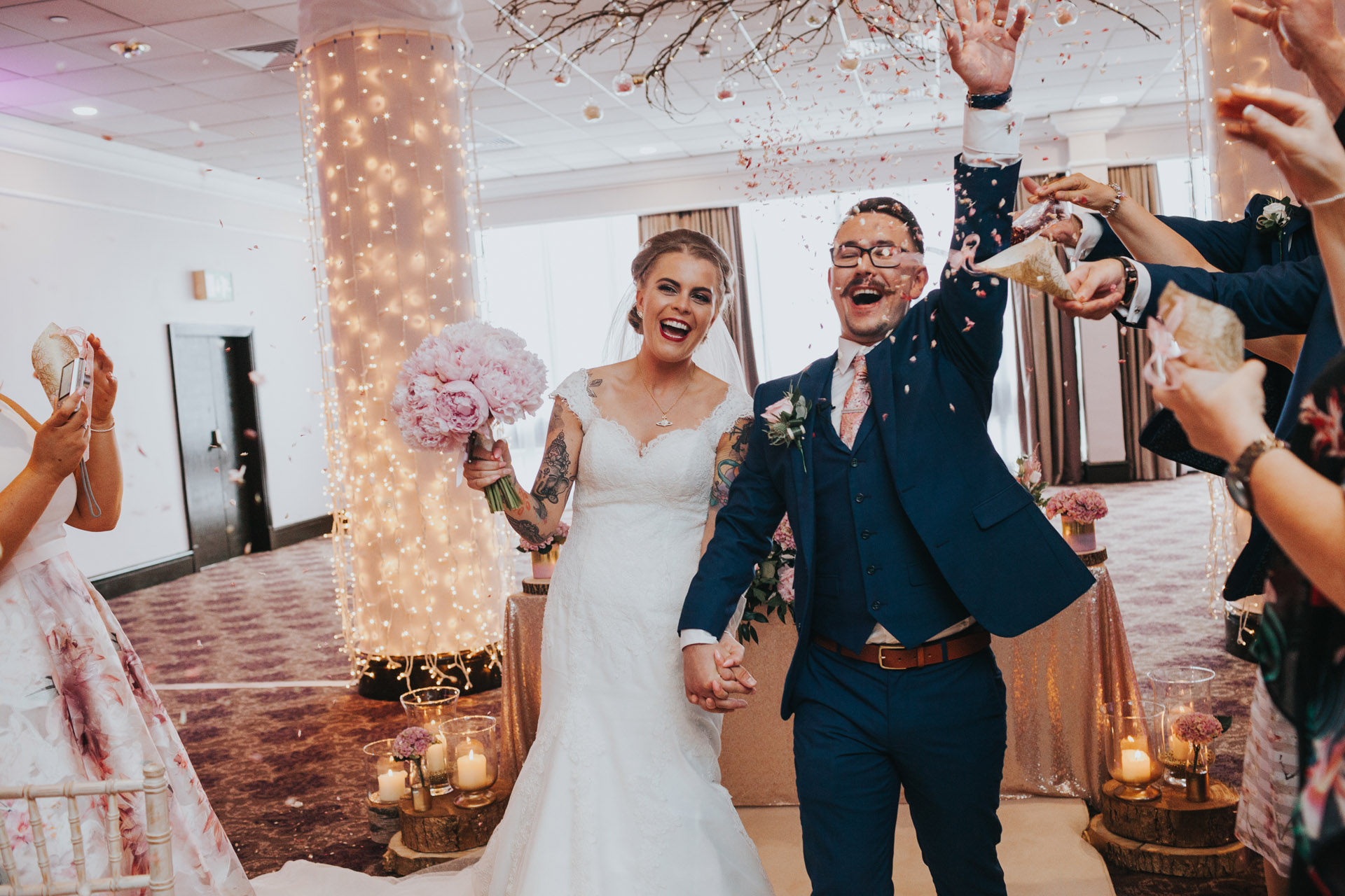 Bride and groom laugh as guests throw confetti. 