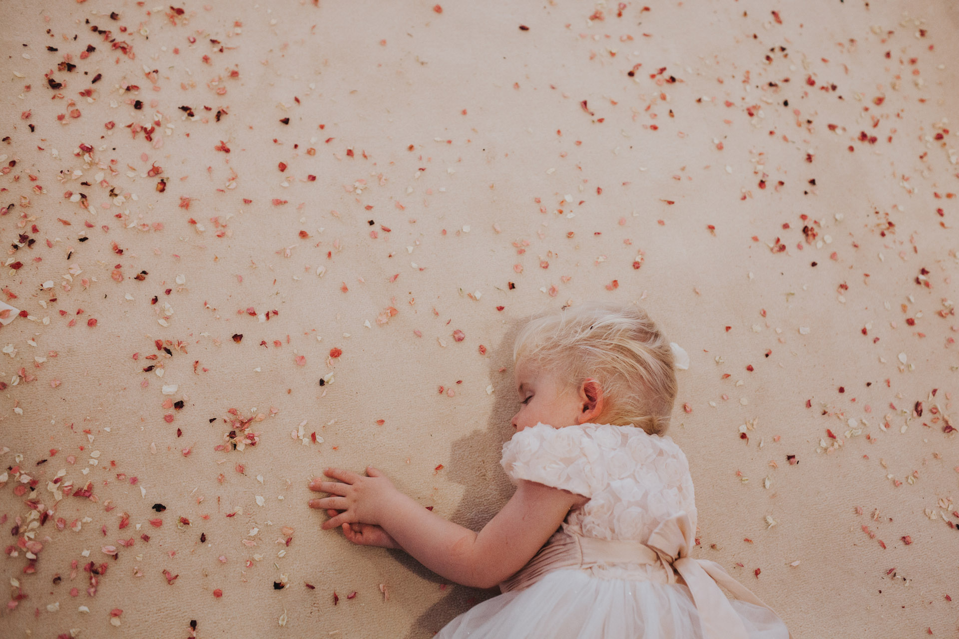 flower girl sleeps on confetti covered floor.