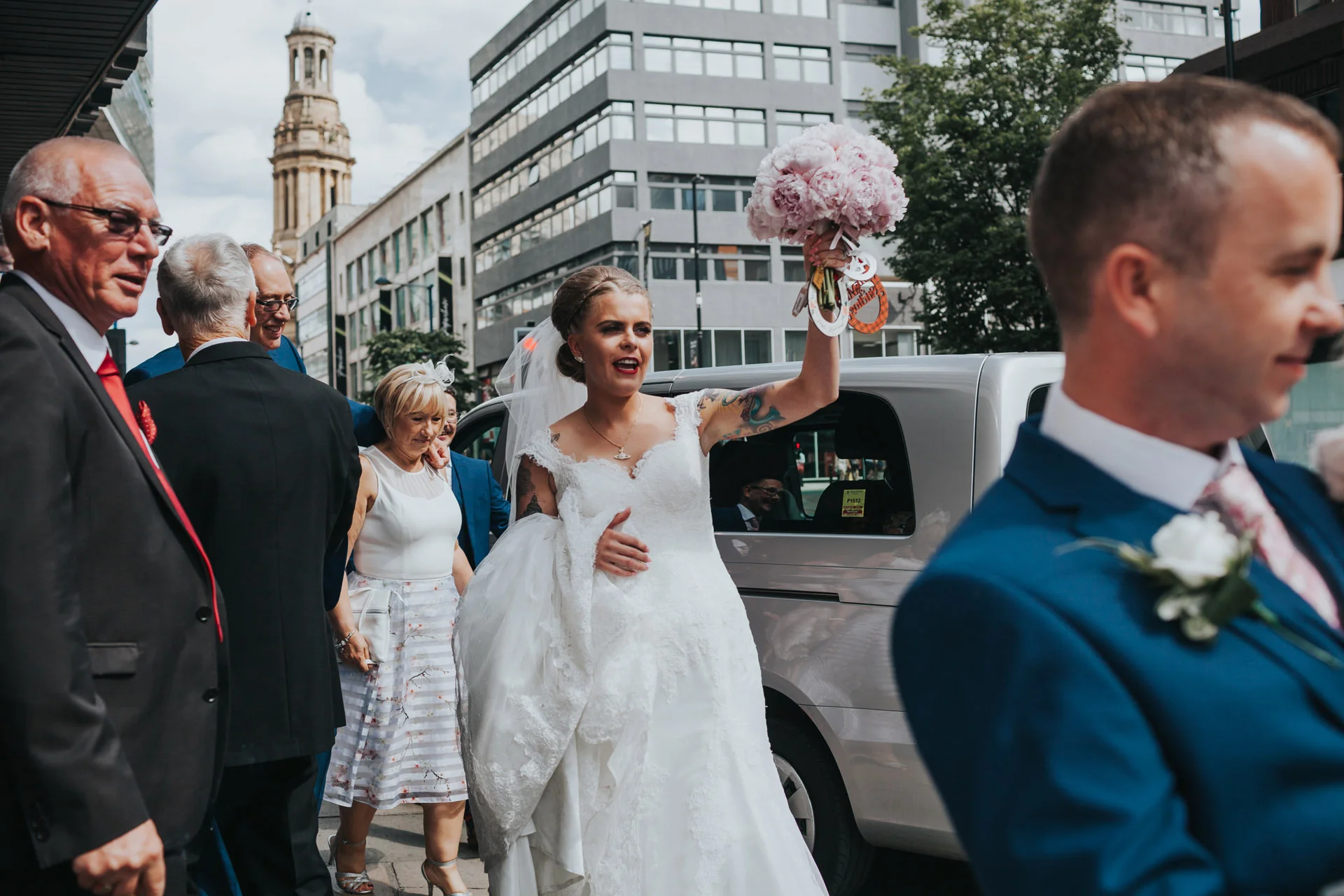 Bride exits Manchester wedding venue holding her bouquet in the air. 