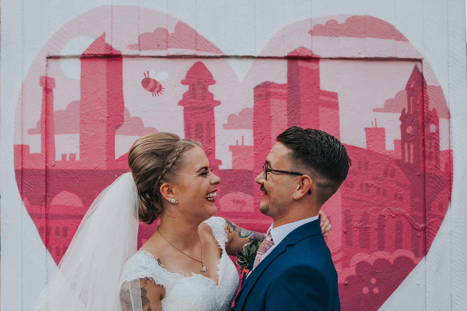 Couple smile in front of heart shaped street art in Manchester's Northern Quarter.