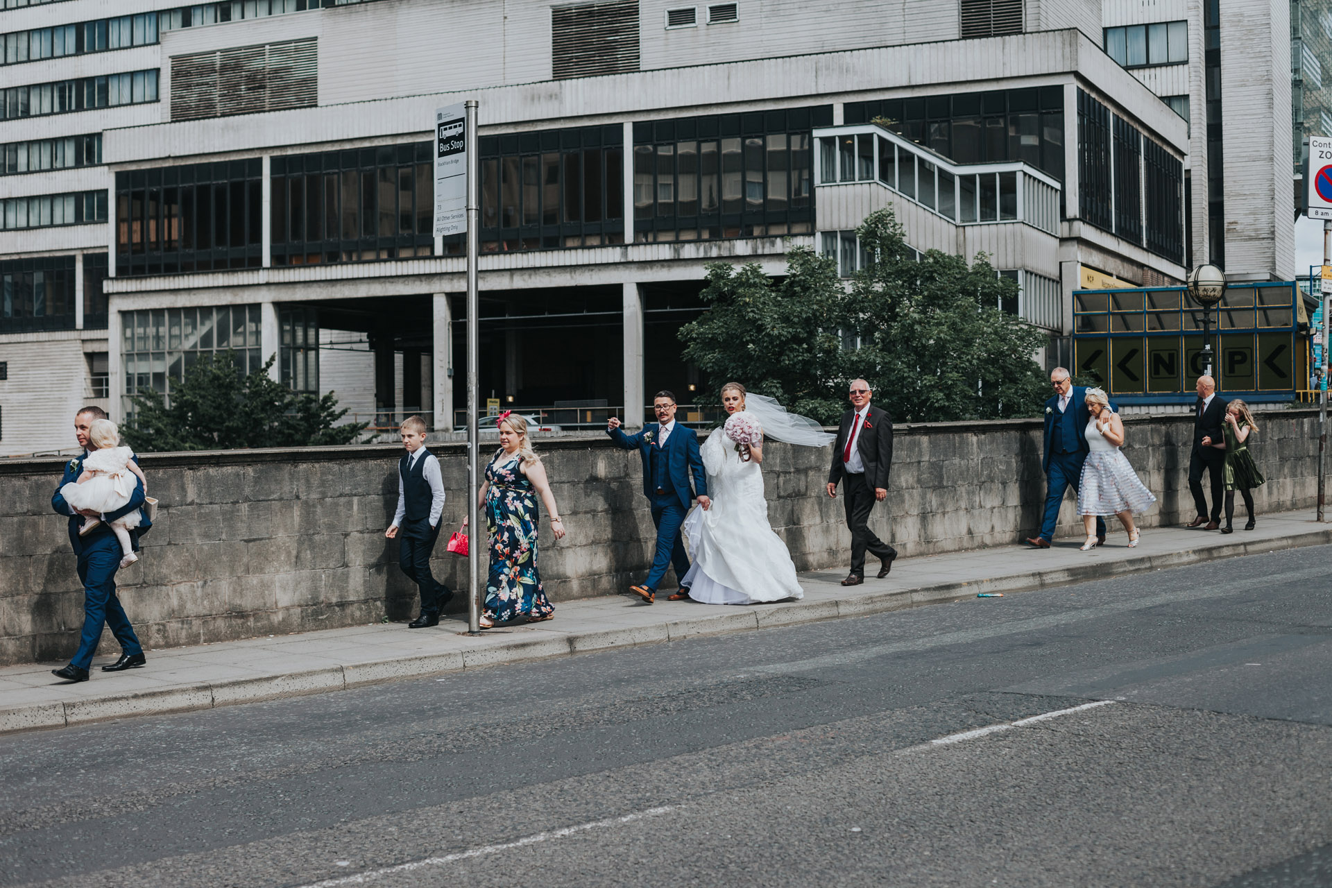 Bride and Groom walk with wedding guests through the streets on Manchester. 