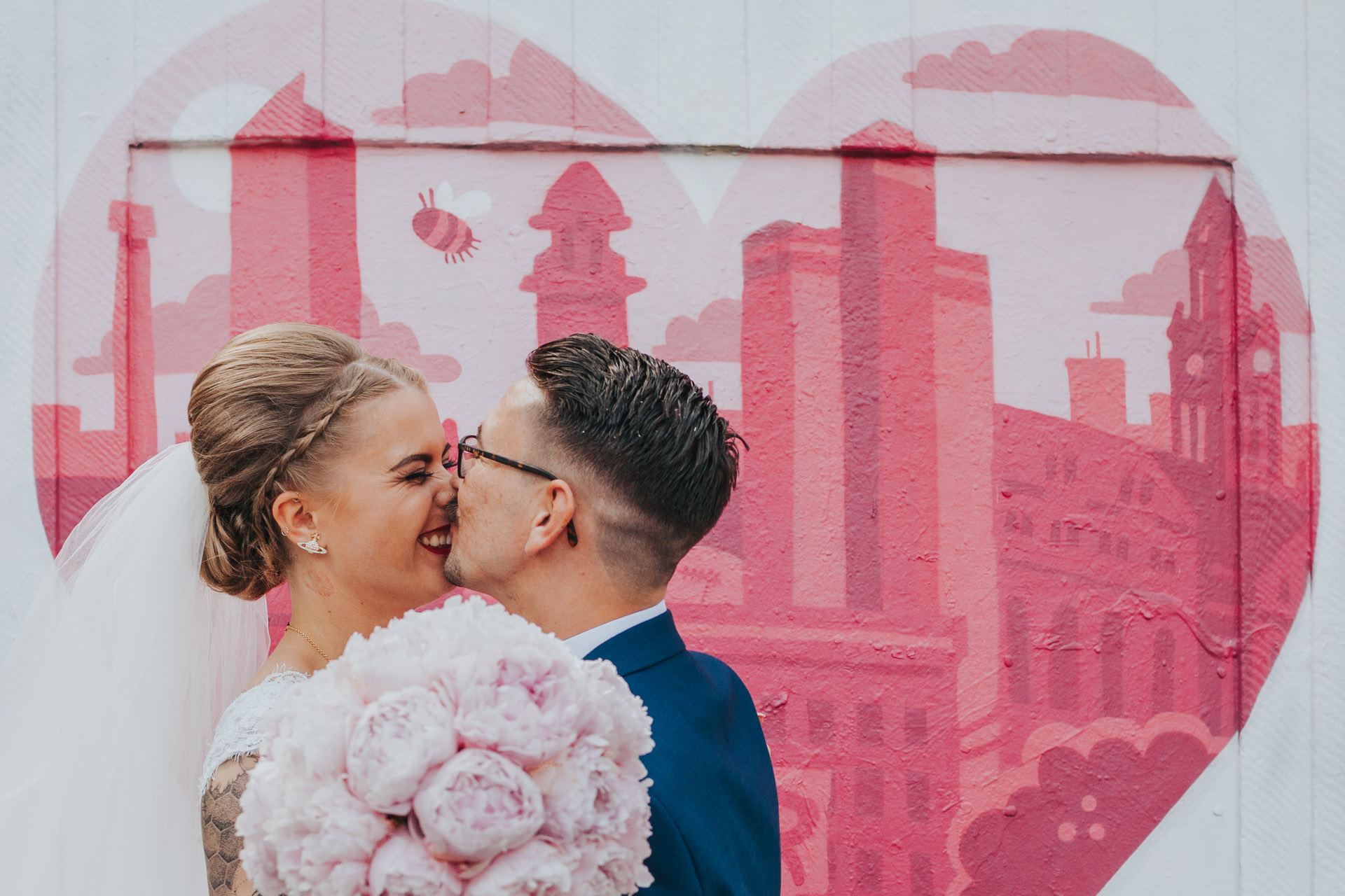 Bride and groom kiss in front of big heart. 