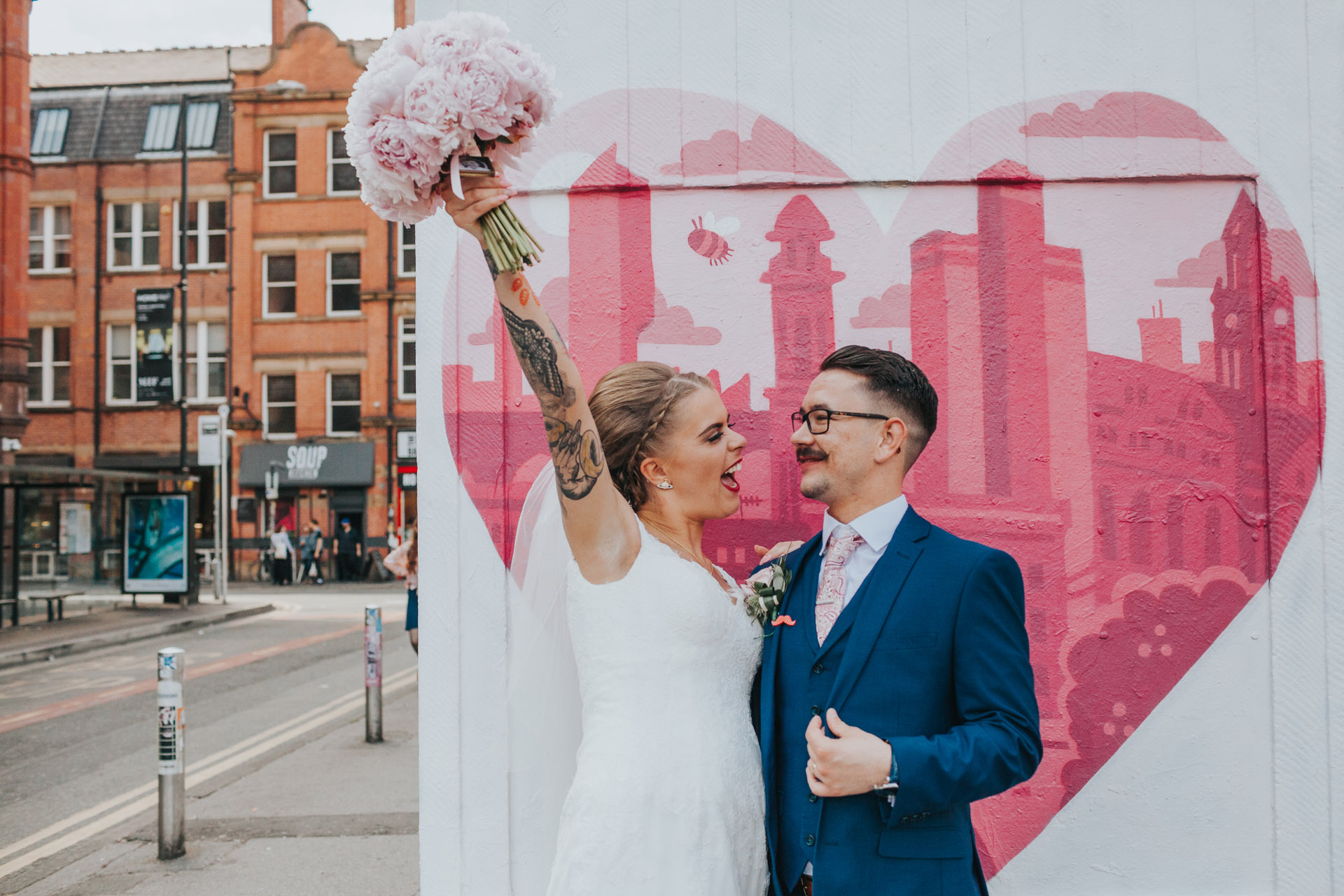 Bride holds flowers up cheering in Manchester's Northern Quarter. 
