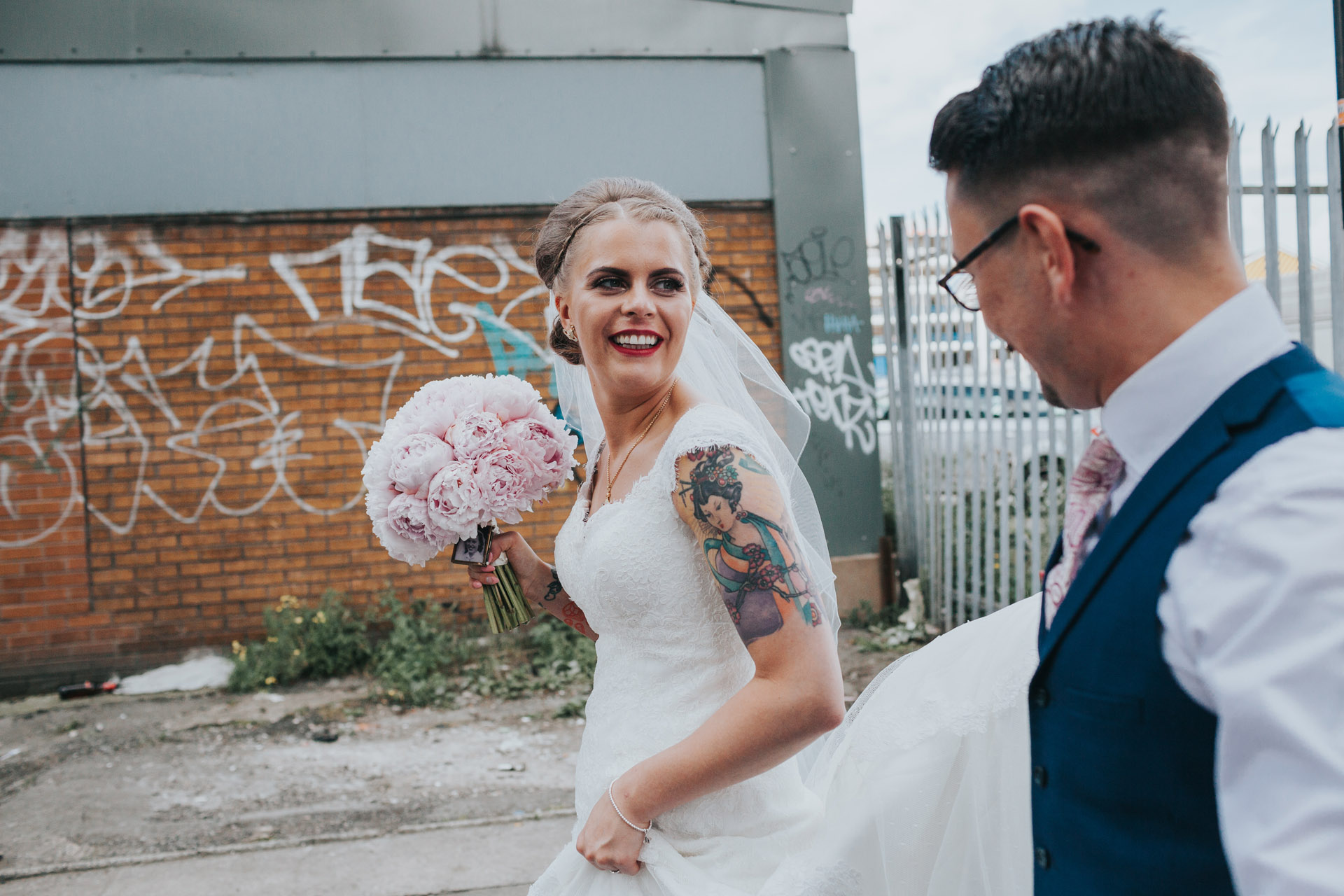 Bride looks to Groom as they walk through Manchester. Graffiti tags in back ground. 