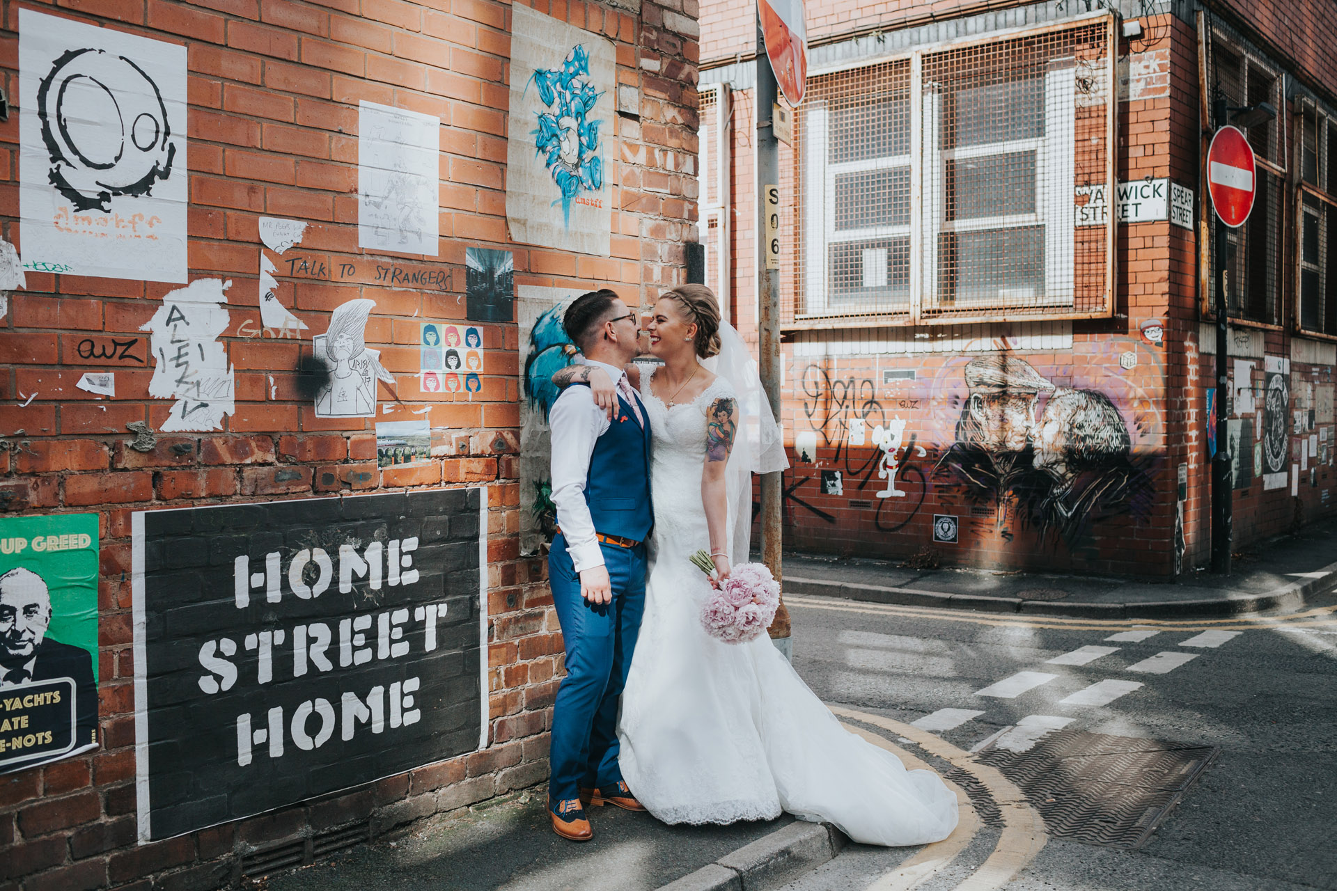 Couple stand laughing together for wedding photographs in front of various street art at Warwick Street, Manchester.