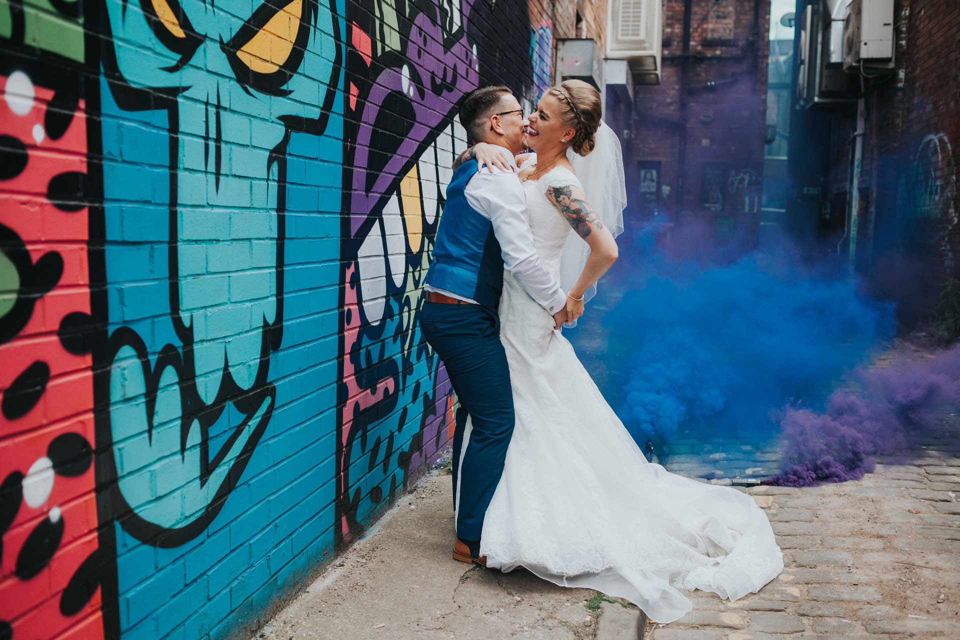 Bride and Groom in front o purple and blue street art with purple and blue smoke bombs, Northern Quarter, Manchester. 