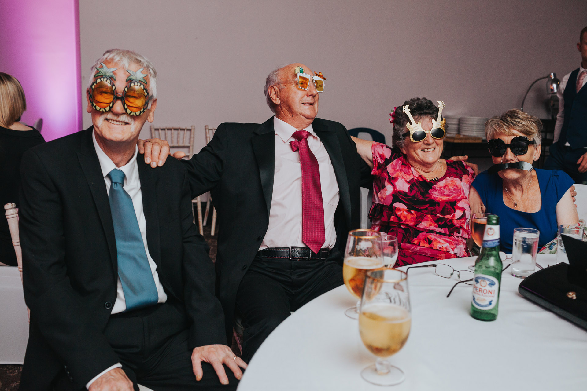 Wedding guests sit at table wearing wacky glasses at Manchester Wedding. 