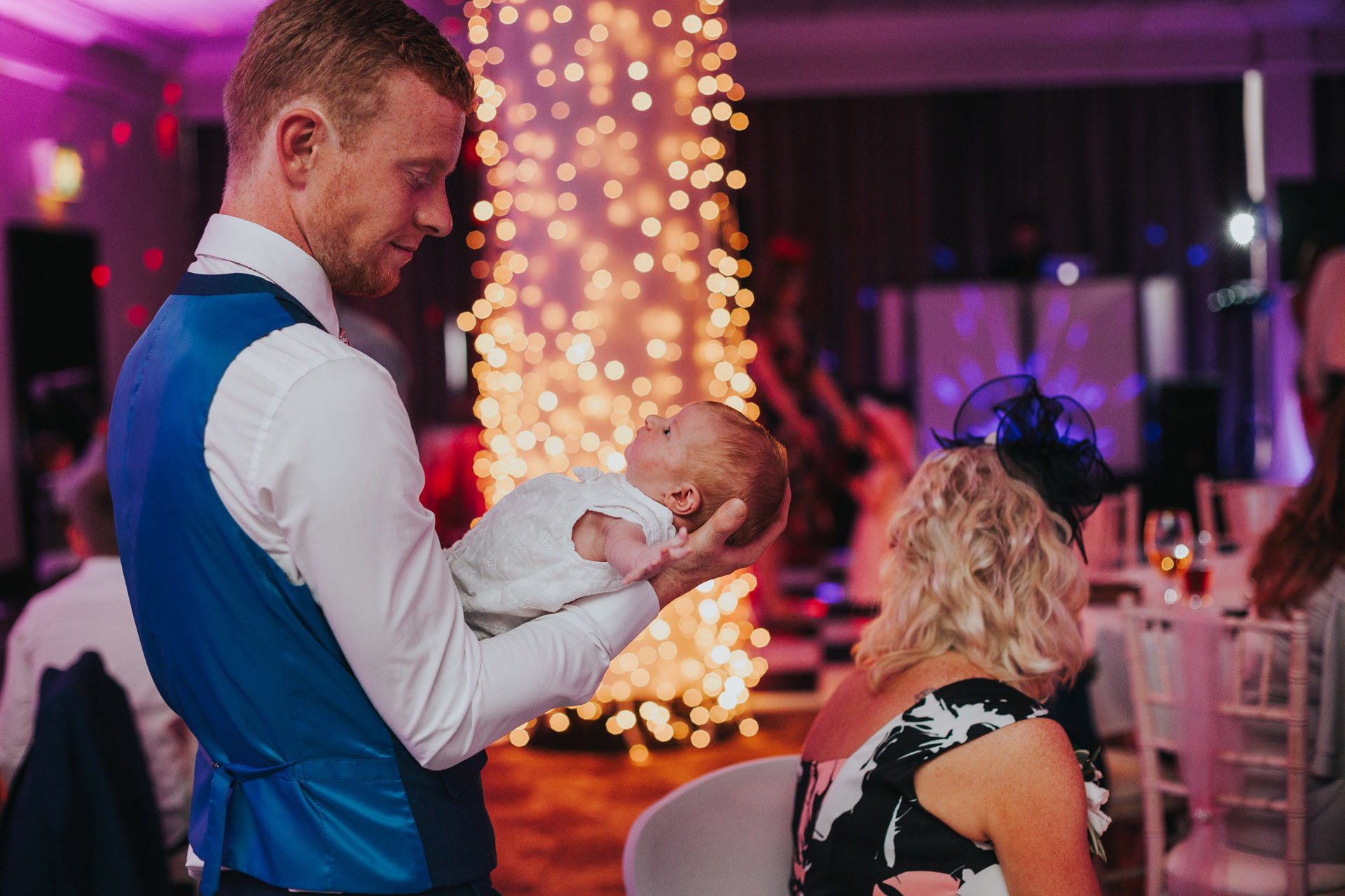 Man holding new born baby at wedding party.