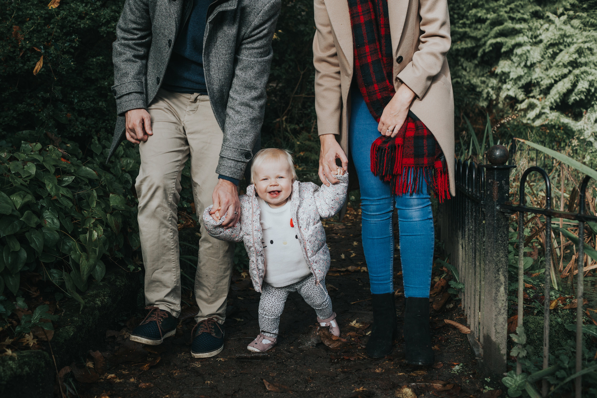 Evie is walking between her Mum and Dad's legs. 