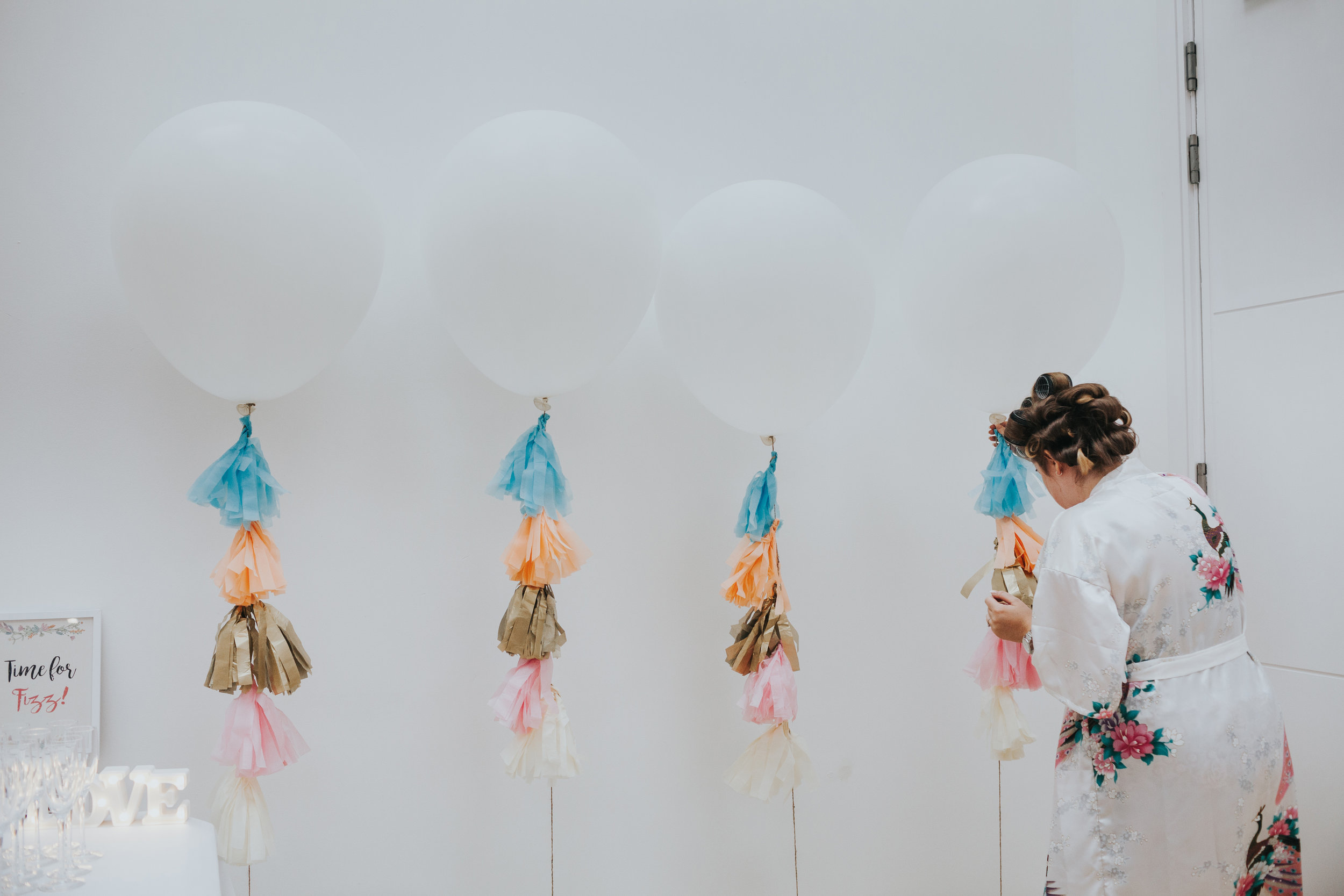 Bride in rollers dresses large white balloons on her wedding day in Liverpool.