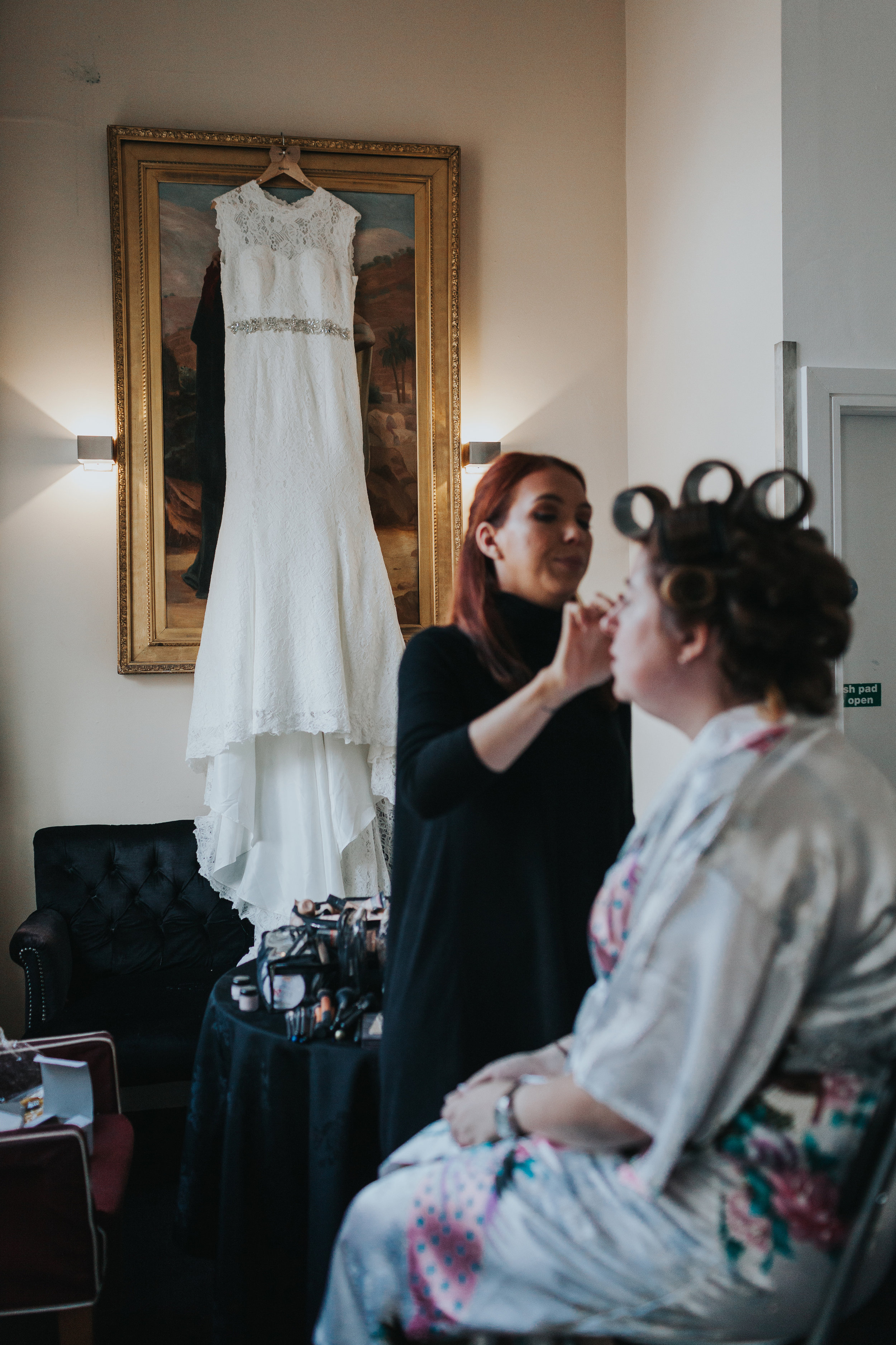 Bride in front of wedding dress getting her make up done. 