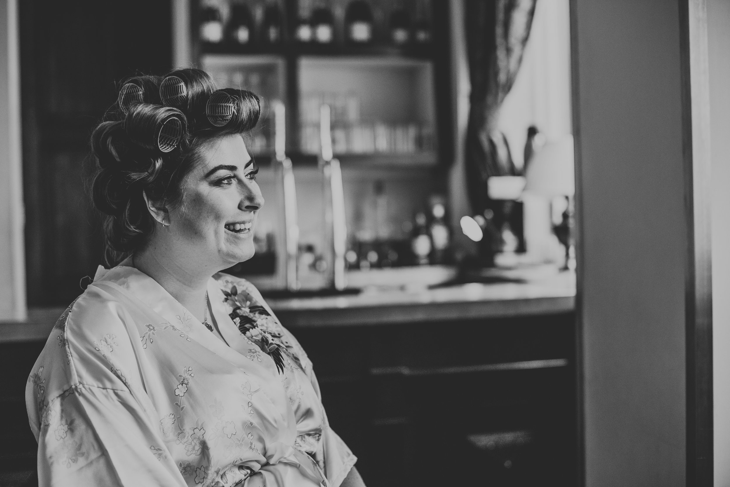 Bride smiling with her rollers in, in front of the bar. 