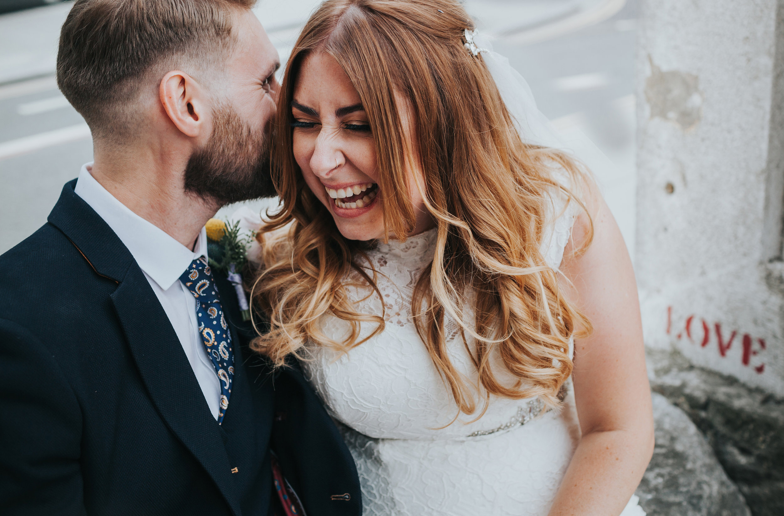 Bride and Groom laugh in front of LOVE street art in Liverpool.
