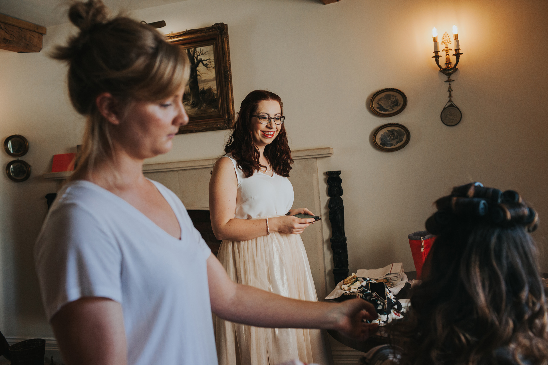 The bridesmaid looks on smiling as the bride has her finishing touches done.