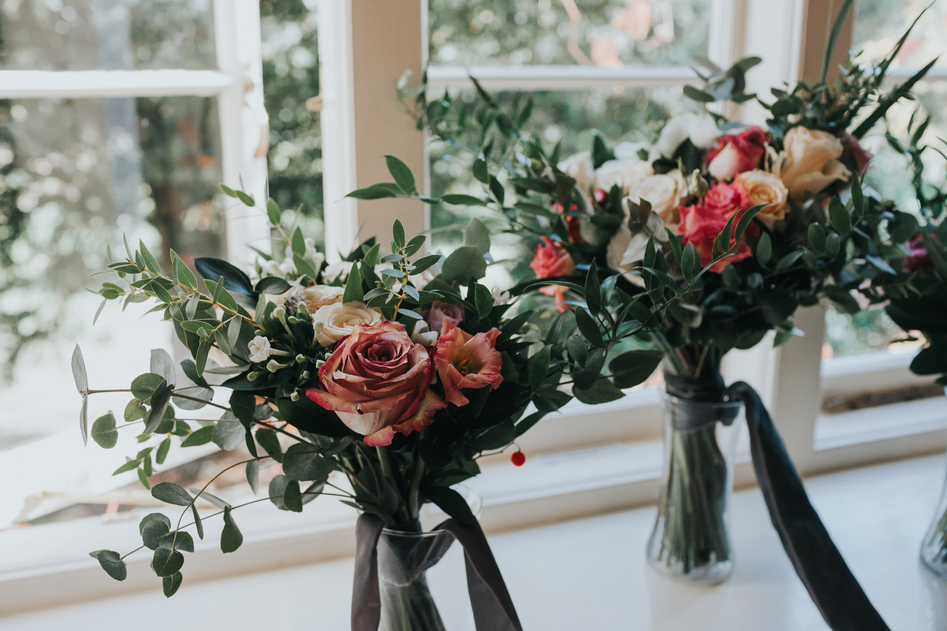 Pink flowers and pale green foliage wait on the windowsill. 