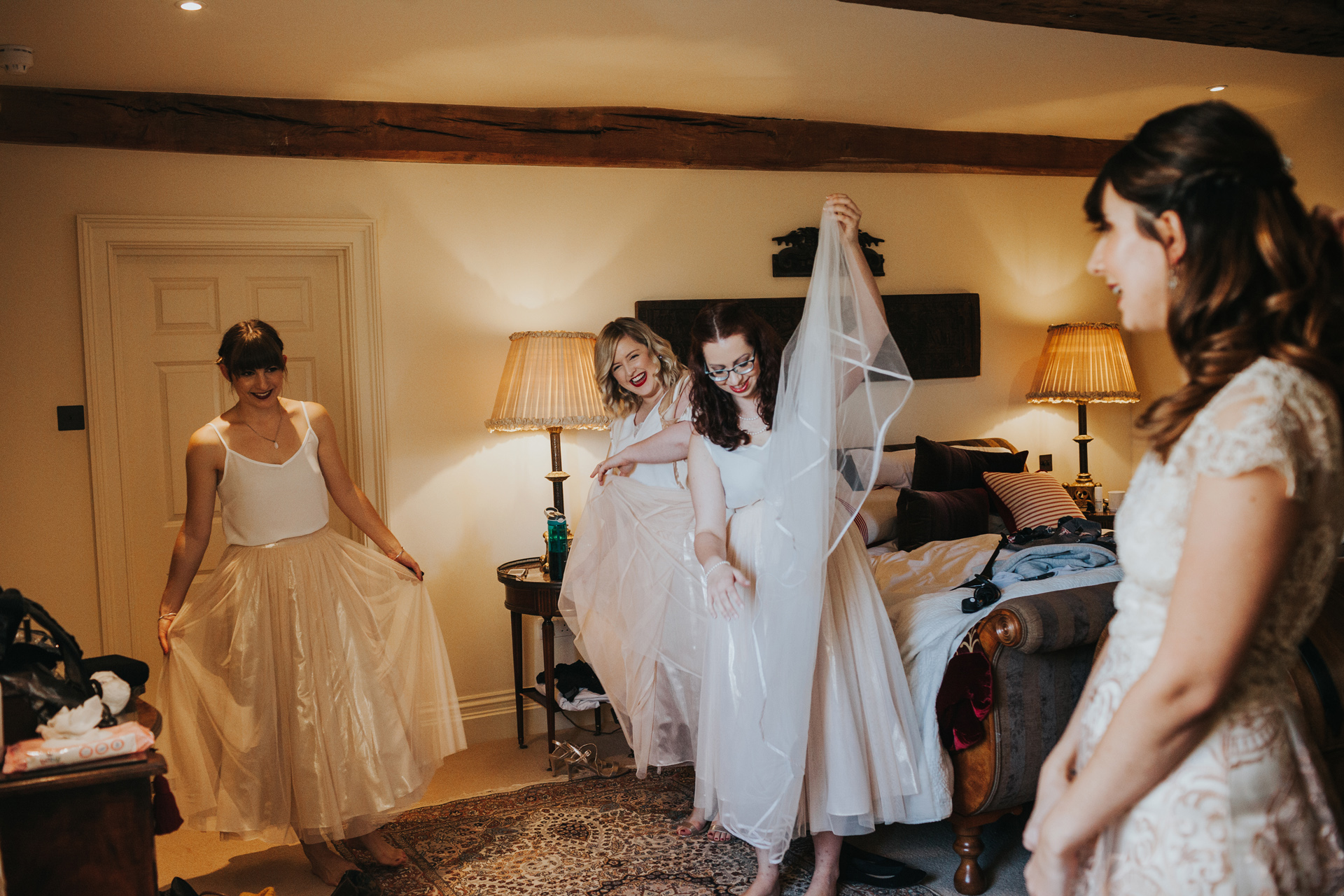 Bridesmaids laughing as one of them moves with the veil towards the bride. 