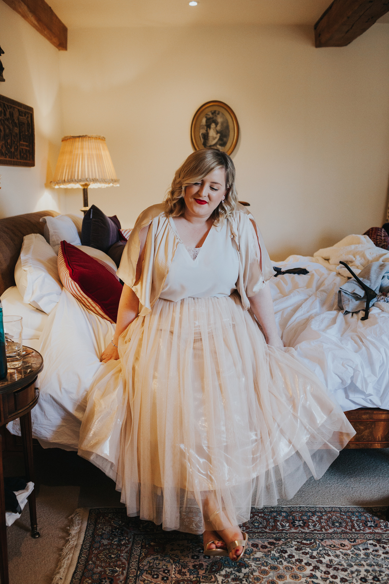 Bridesmaid sits on bed looking content with herself. 