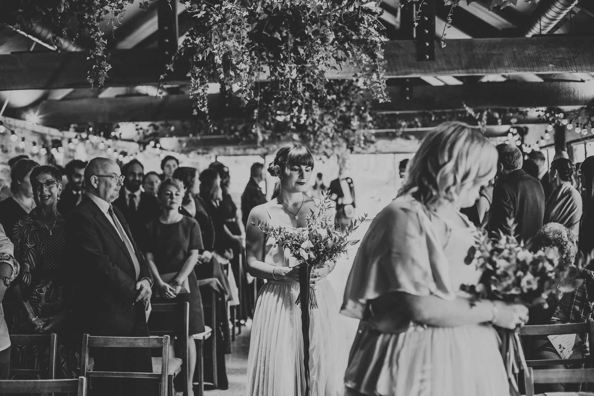 Third bridesmaid walks down the aisle. Photograph in black and white. 