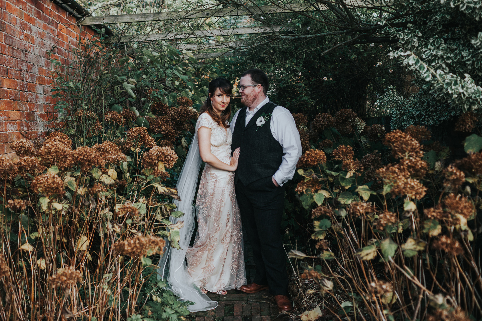 Bride and groom stand together in a sea of browning hydrangeas. 