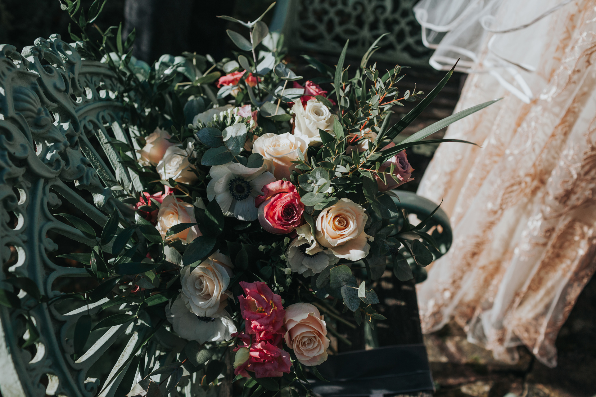 Wedding flowers sit on teal iron chair with wedding dress in the back ground.