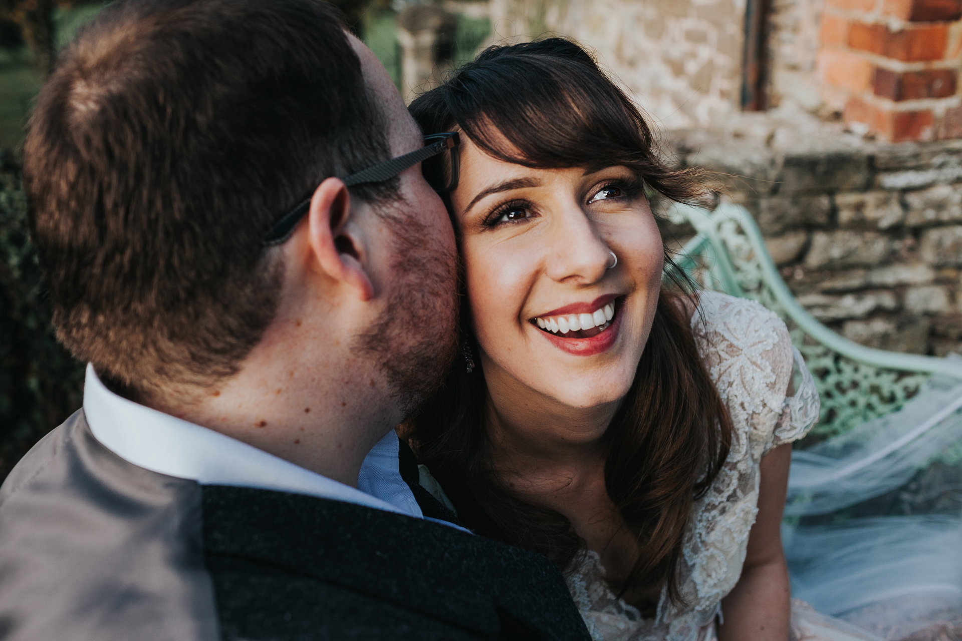 Bride smiles as groom whispers something in her ear. 