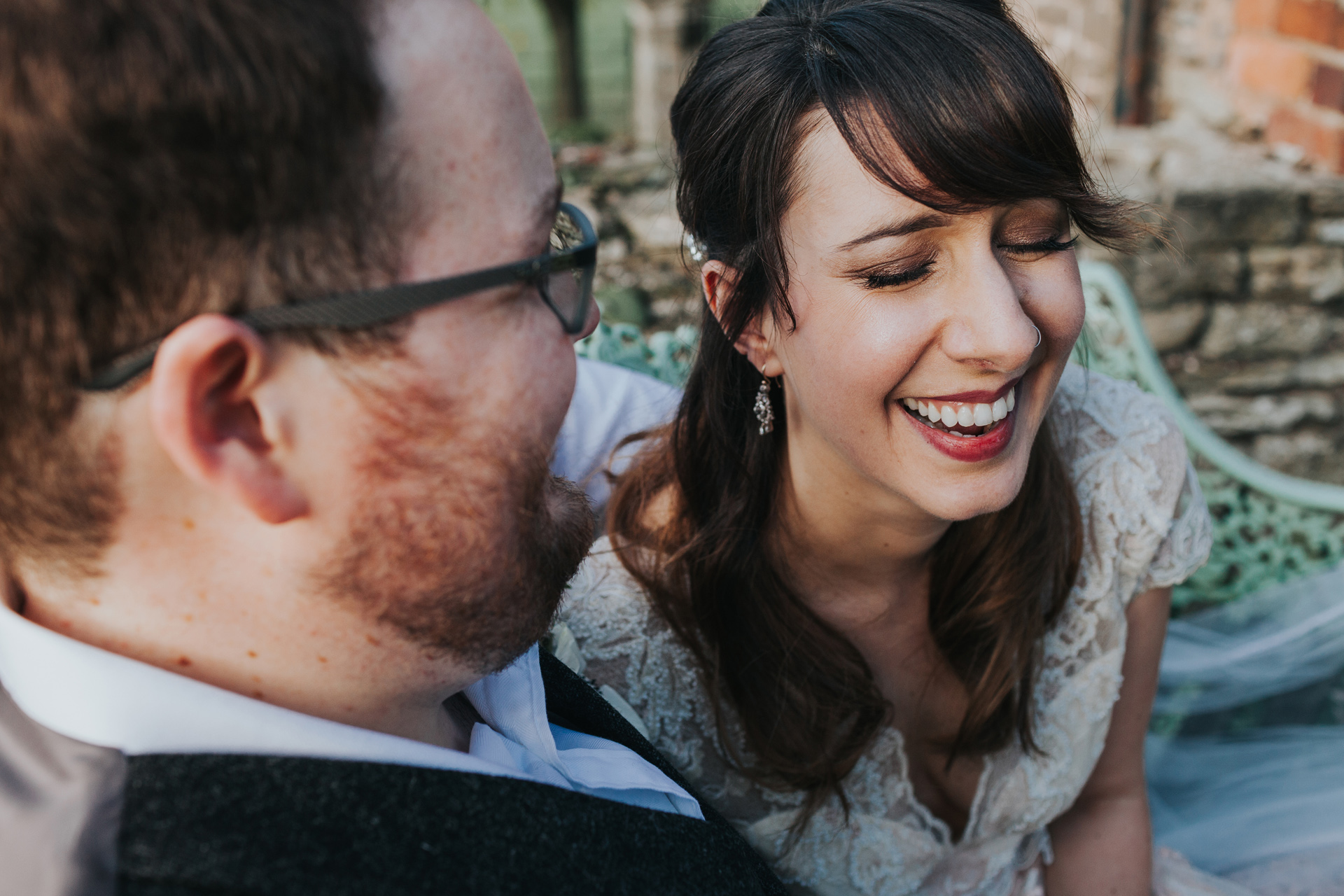 Bride laughs as groom whispers something in her ear. 