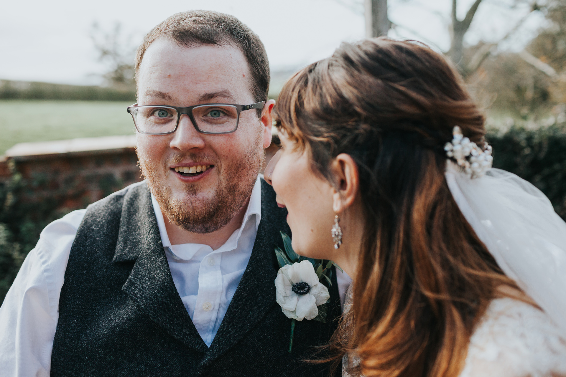 Groom looks surprised as bride whispers to him. 