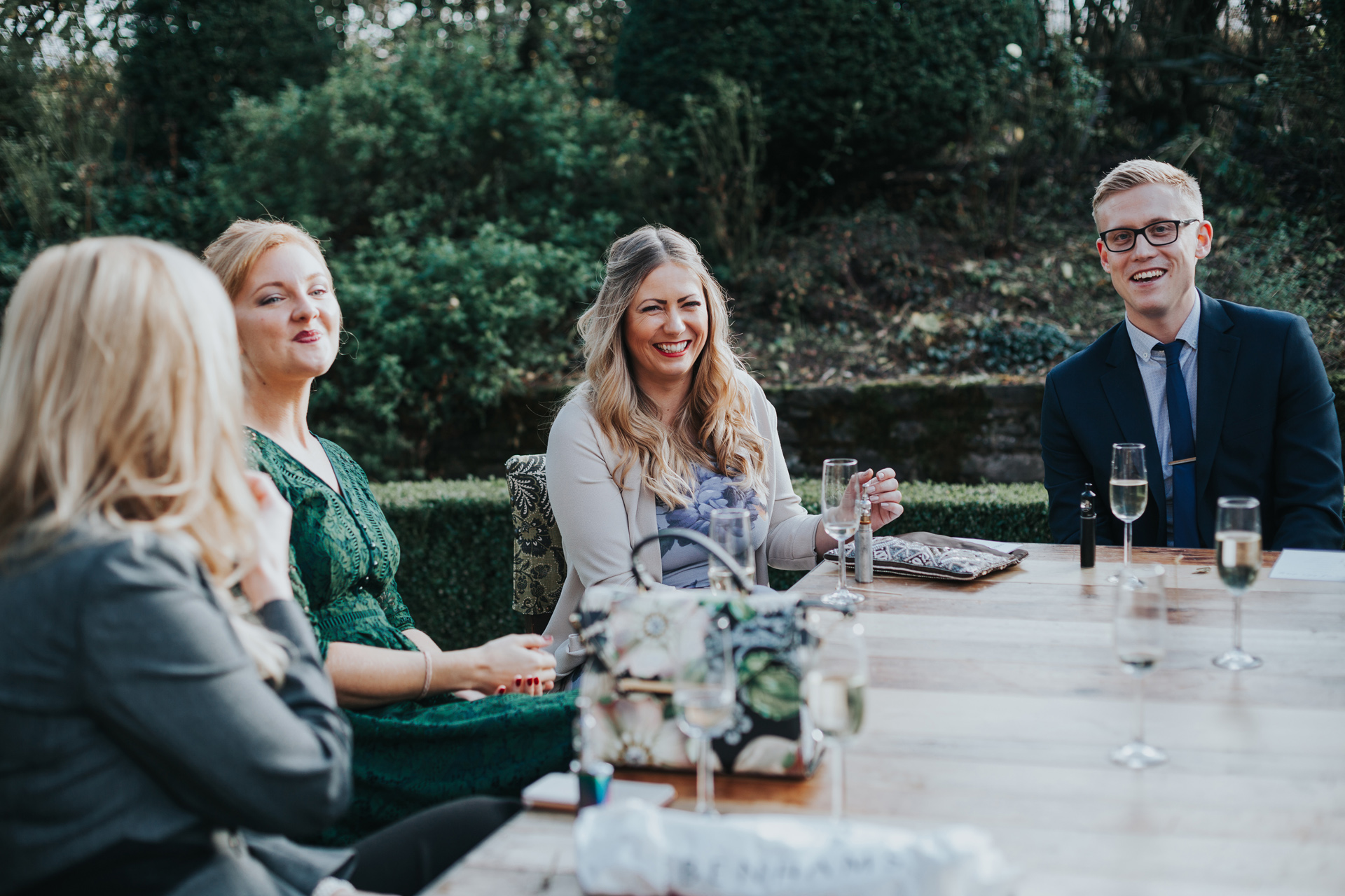 Wedding Guests sitting at table in garden laughing at Dewsall Court. 