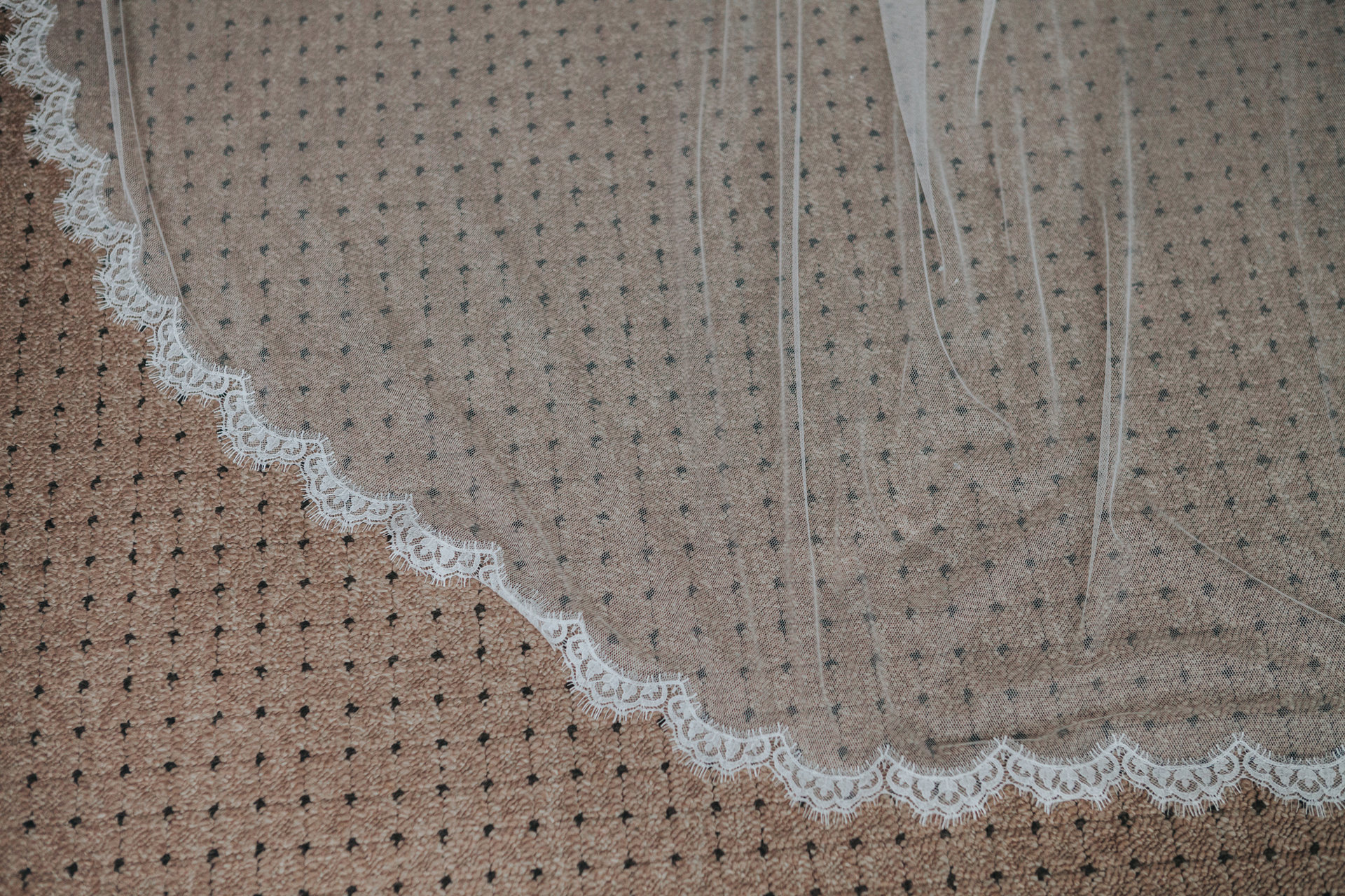 Close up of the edge of the veil resting on the carpet. 