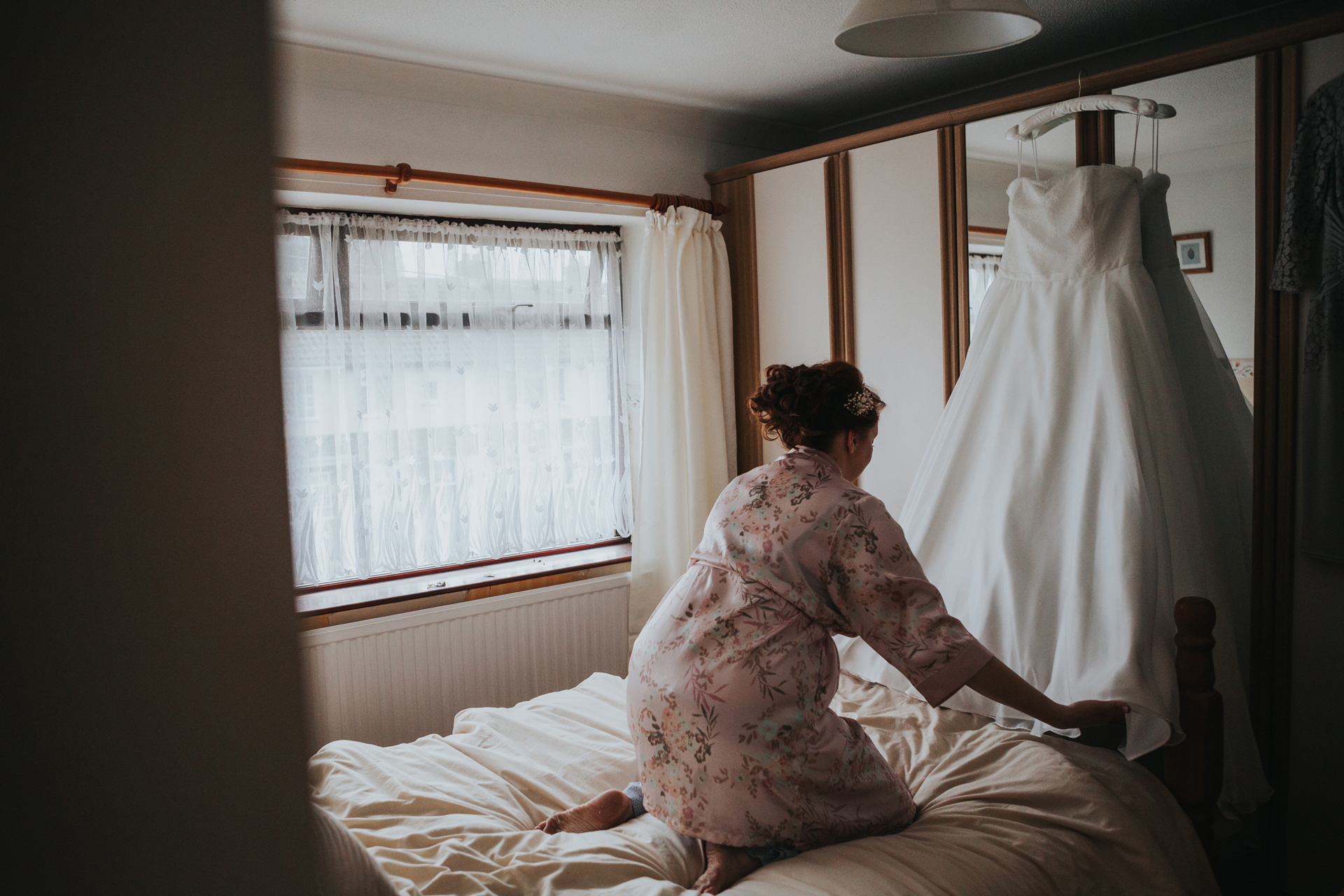 Bride hanging her dress up on a wardrobe and fixing the bottom of the dress.